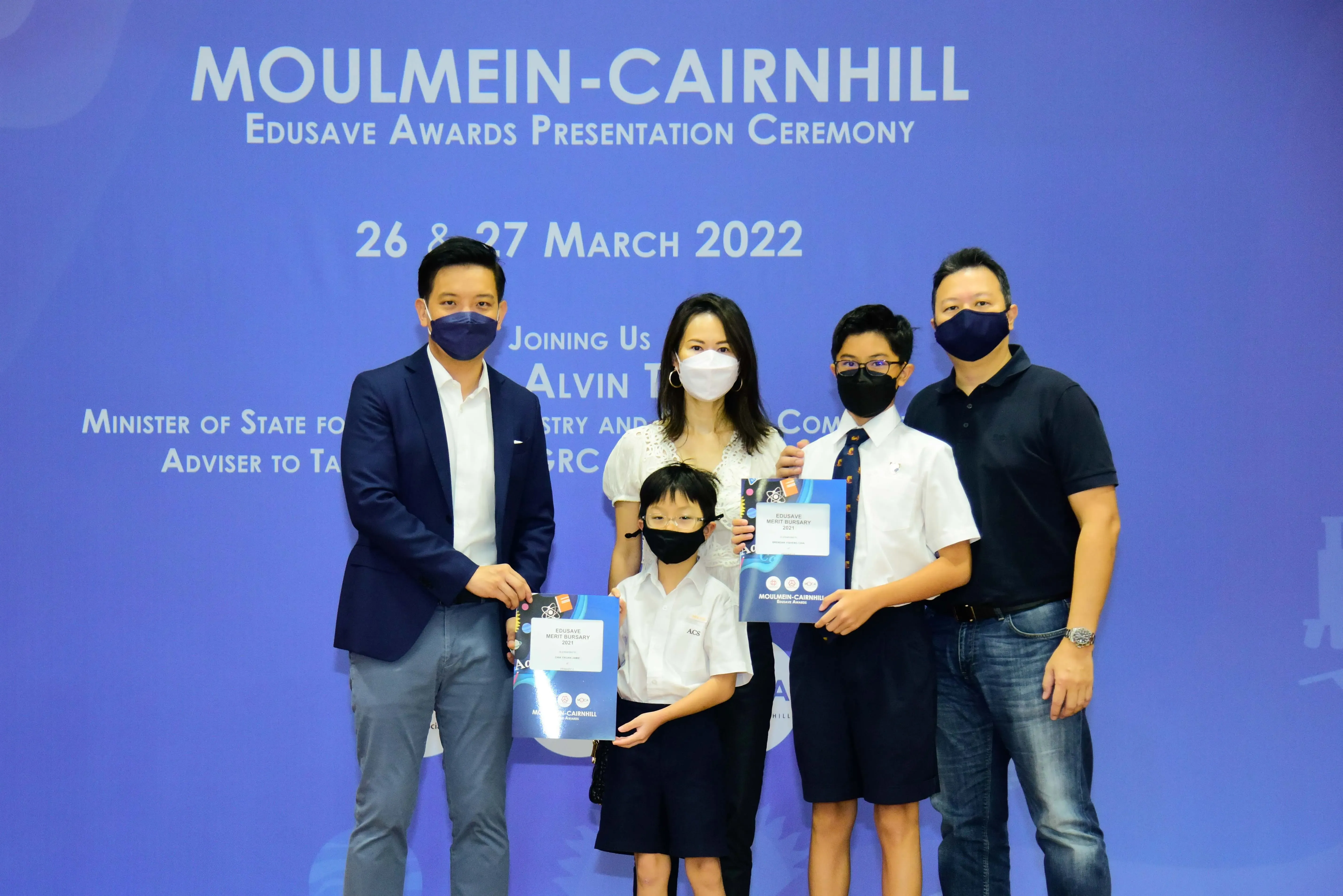 Five masked people pose at the Moulmein-Cairnhill Edusave Awards Ceremony on 26-27 March 2022, two children holding award folders.