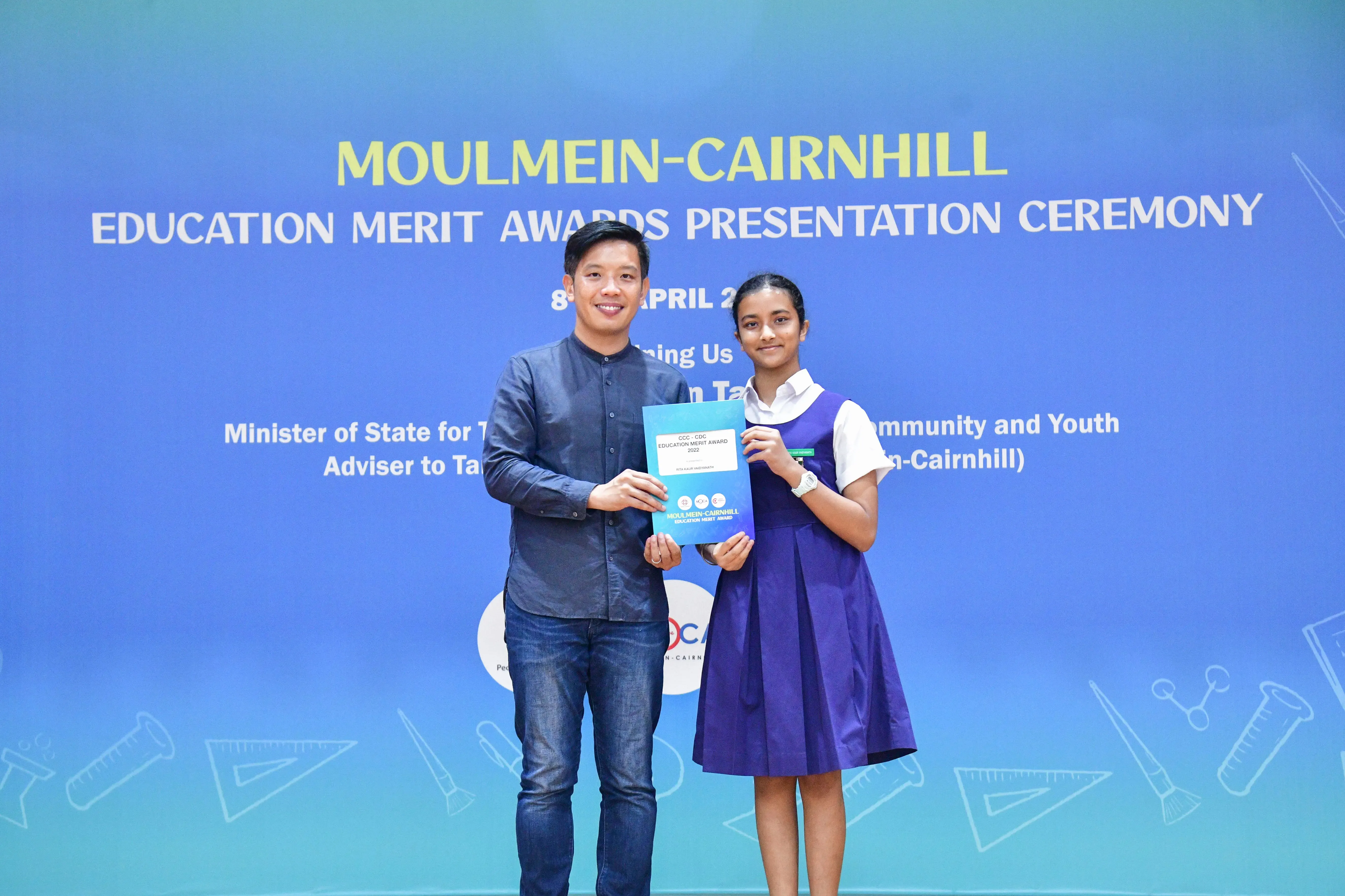 A man and a girl in school uniform hold an award certificate at the Moulmein-Cairnhill Education Merit Awards ceremony.