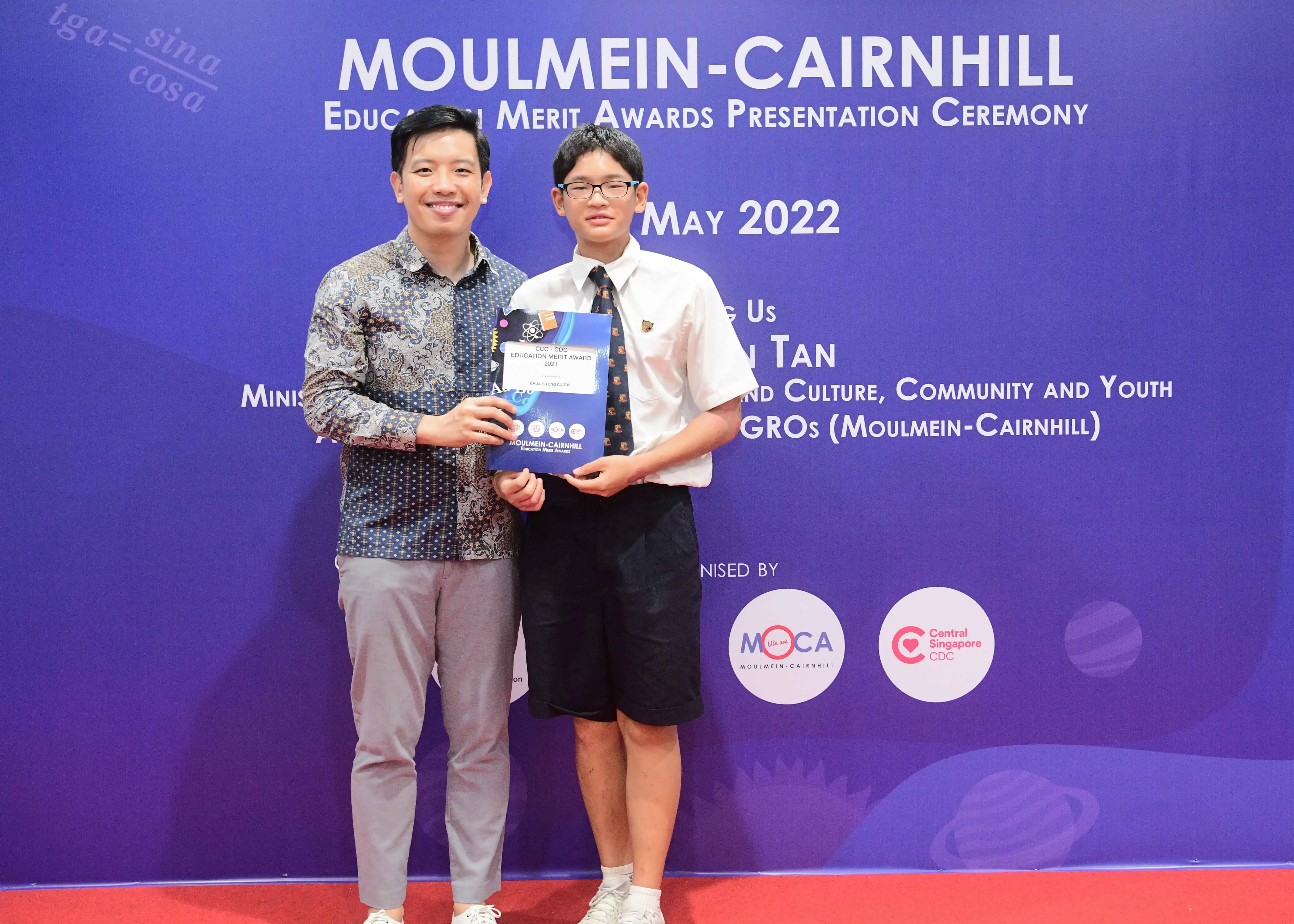 Two people pose holding an award certificate at the Moulmein-Cairnhill Education Merit Awards Ceremony, May 2022.