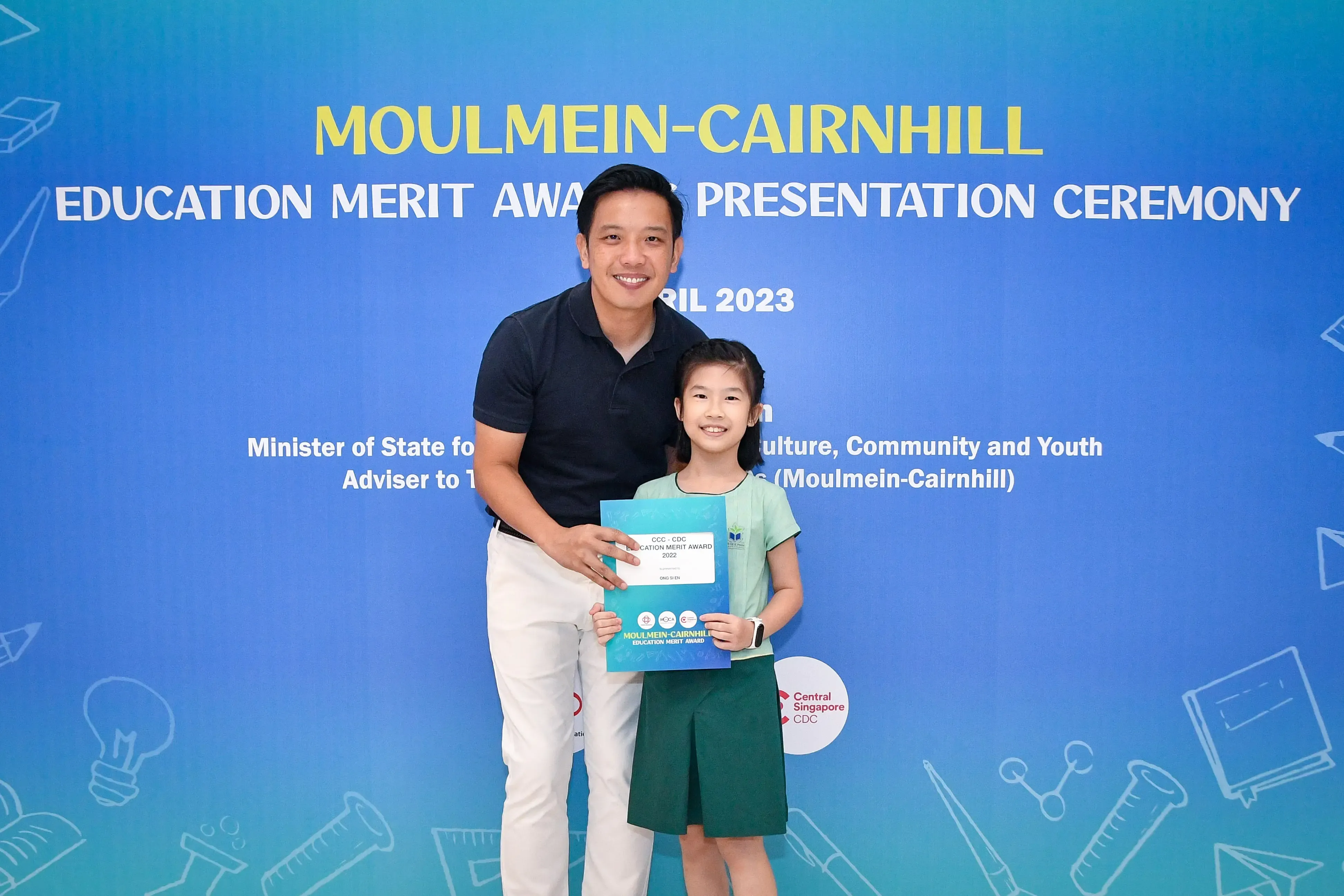 A man and a young girl holding an award certificate at the Moulmein-Cairnhill Education Merit Award Ceremony 2023.
