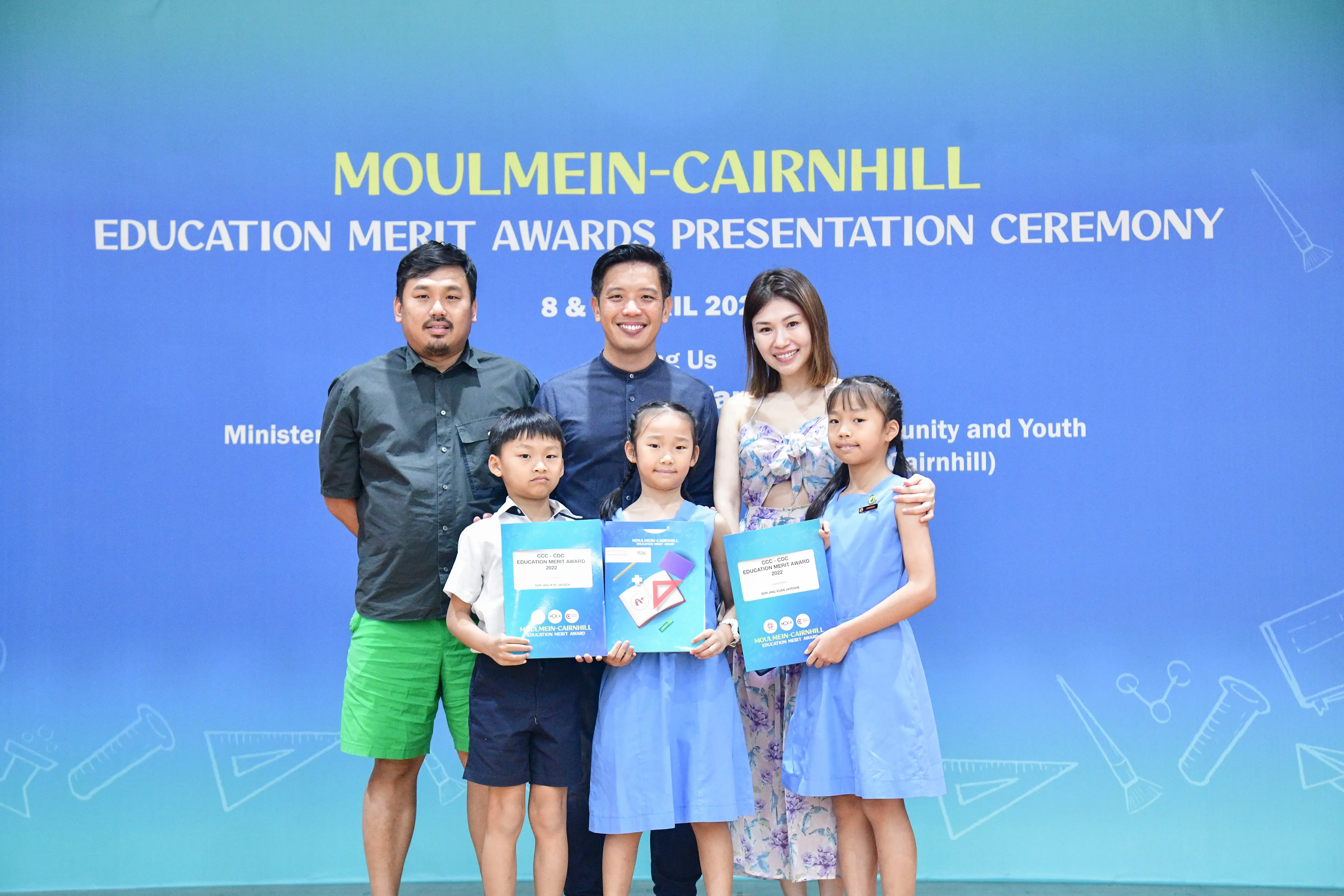 Three adults and three children pose holding award folders at the Moulmein-Cairnhill Education Merit Awards Ceremony.