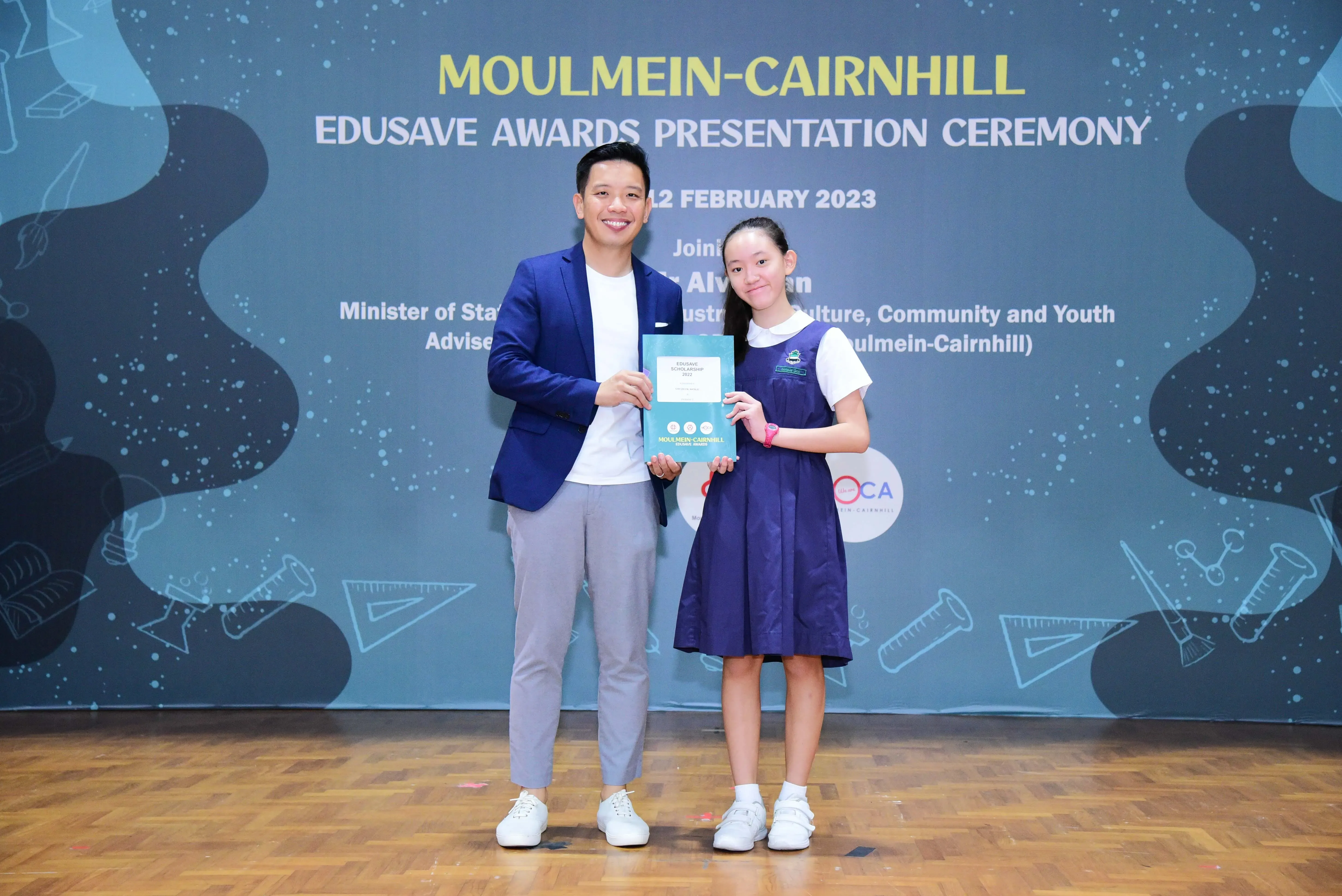 A man and a young girl hold an award certificate at the Moulmein-Cairnhill Edusave Awards Ceremony, February 2023.
