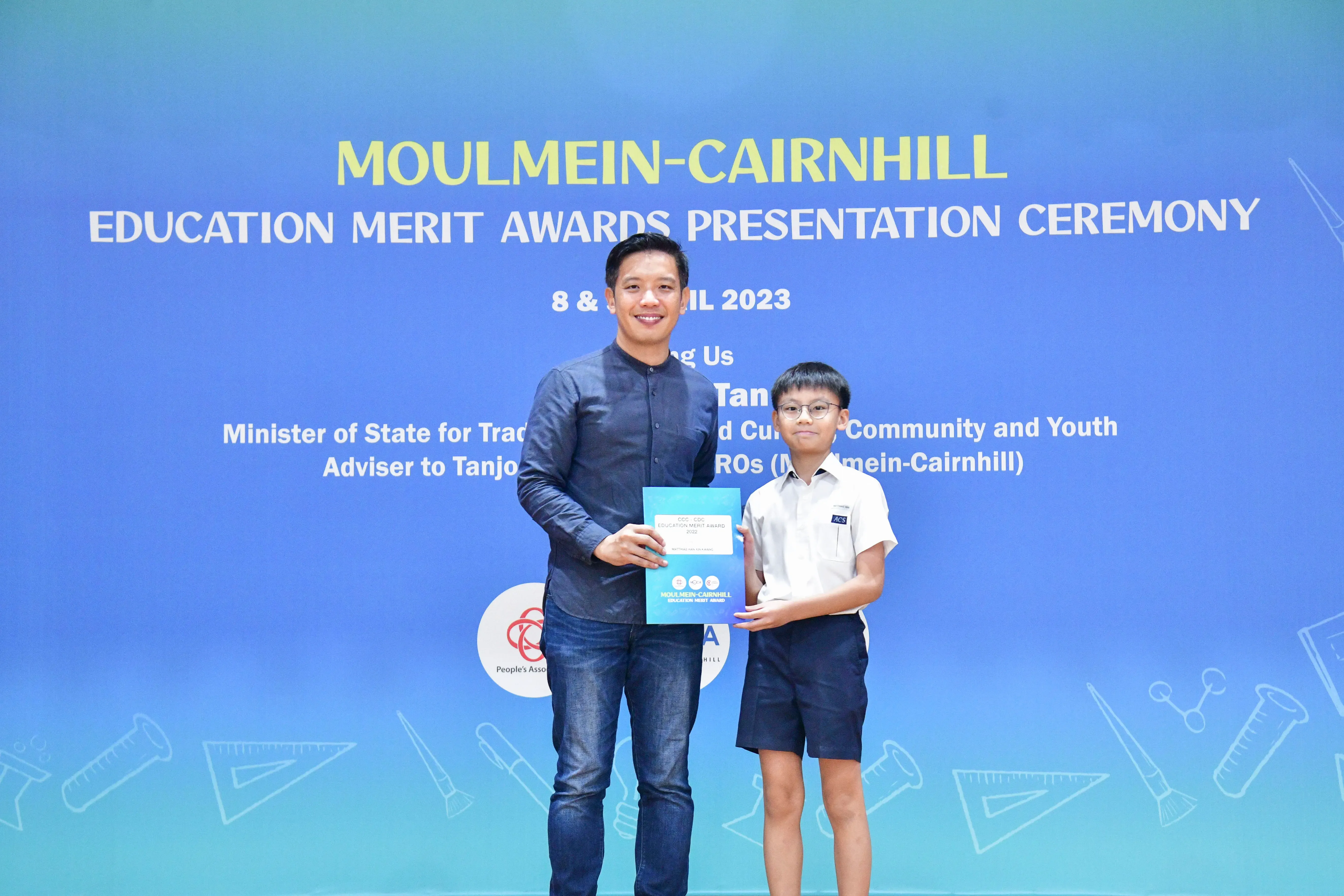 An adult man and a young boy in school uniform pose together holding a certificate at the Moulmein-Cairnhill Education Merit Awards 2023.