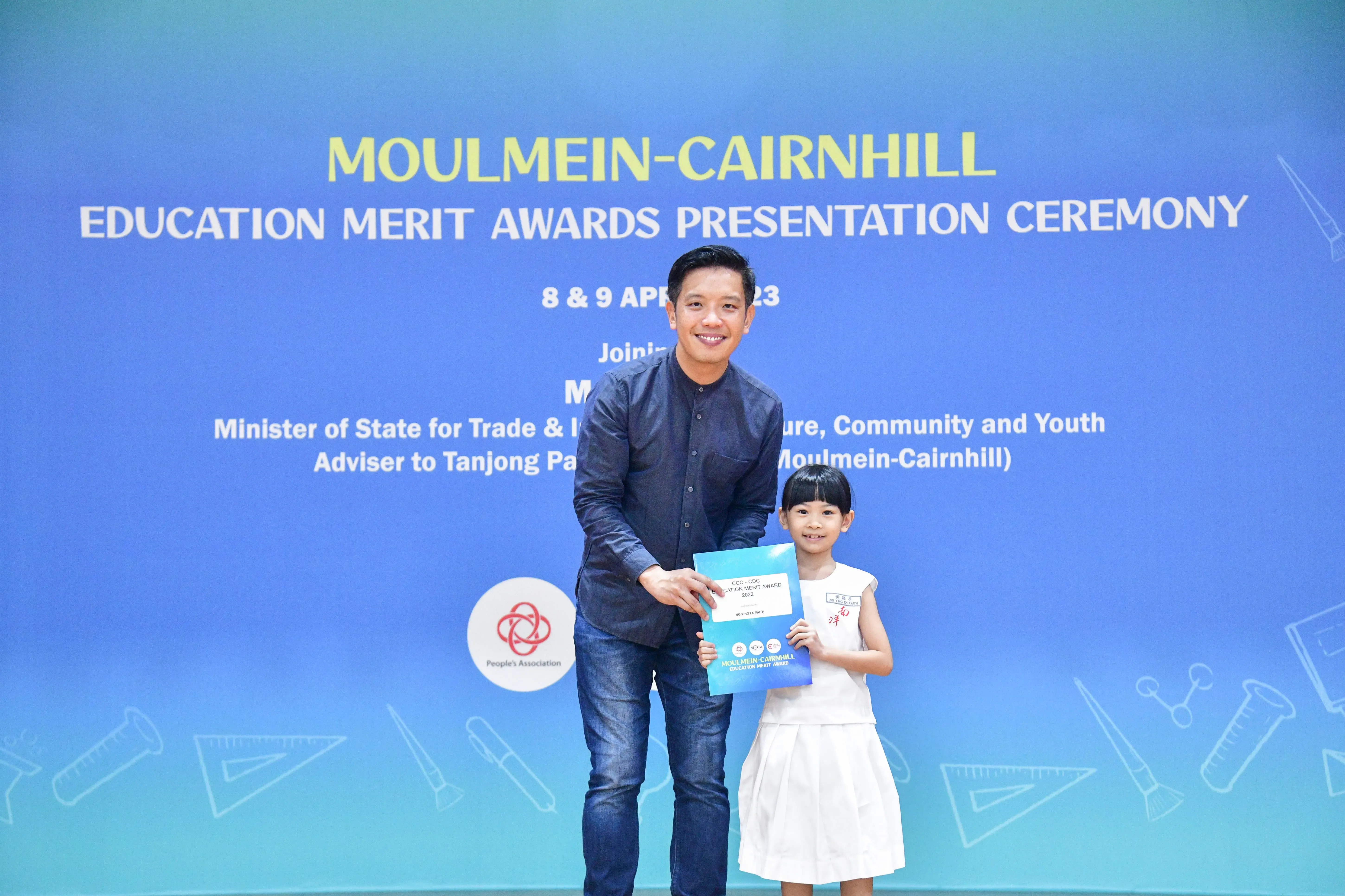 A man and a young girl hold a certificate together at the Moulmein-Cairnhill Education Merit Awards Presentation Ceremony.