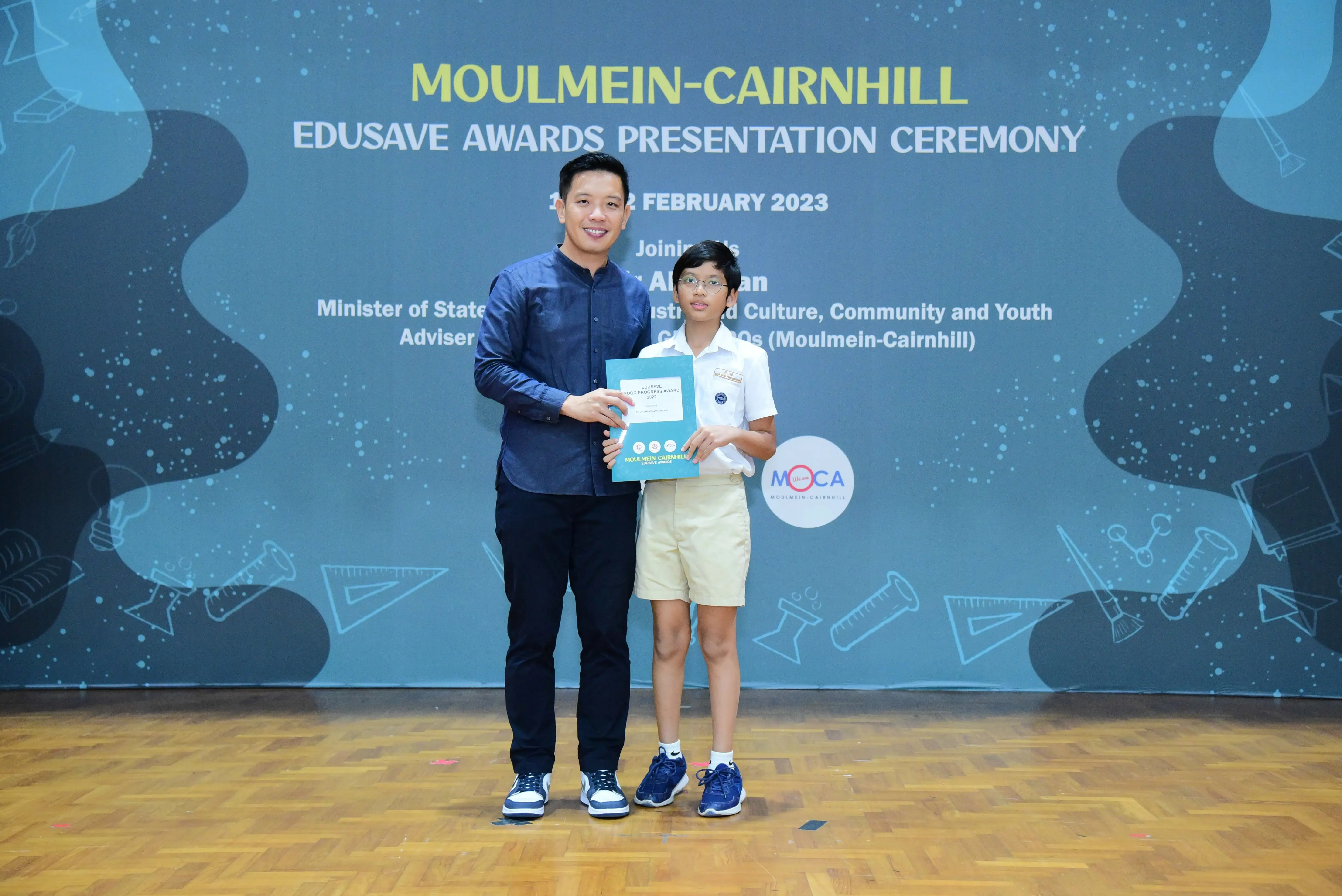 An adult and a young student hold a certificate at the Moulmein-Cairnhill Edusave Awards Ceremony, February 2023.
