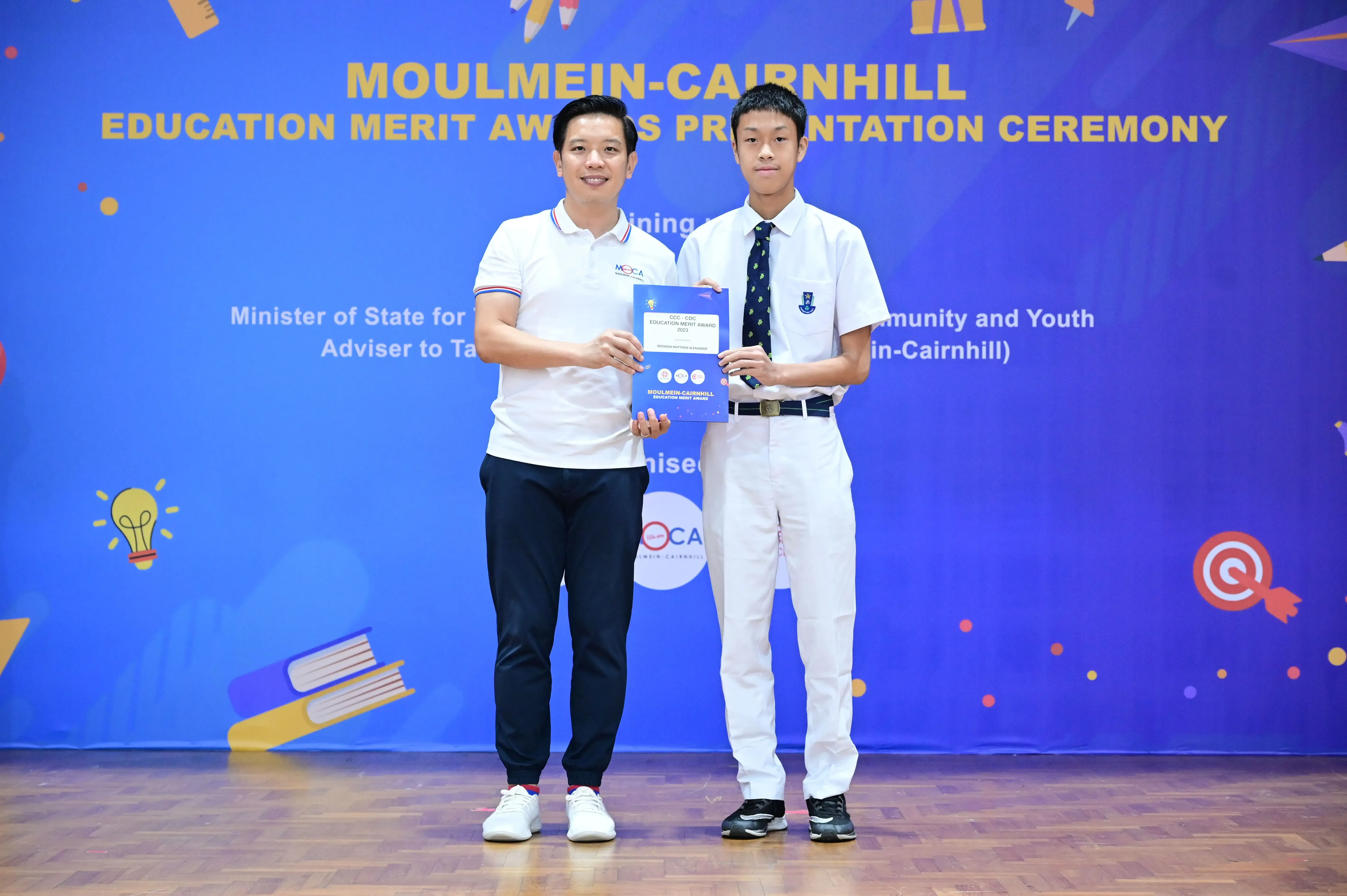 Two people hold an award certificate at the Moulmein-Cairnhill Education Merit Awards Presentation Ceremony.