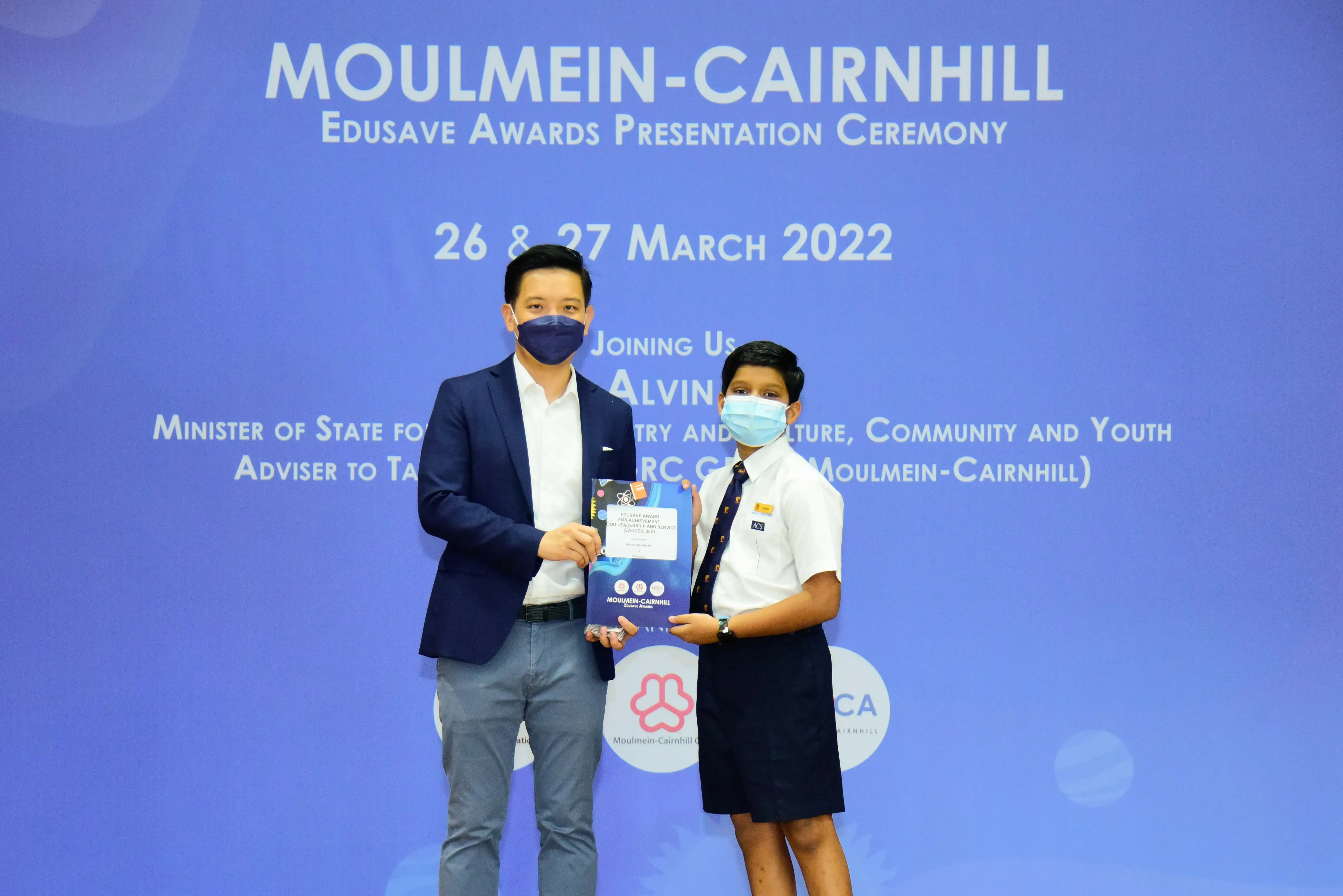 Two masked individuals hold an award folder at the Moulmein-Cairnhill Edusave Awards Ceremony, March 2022.