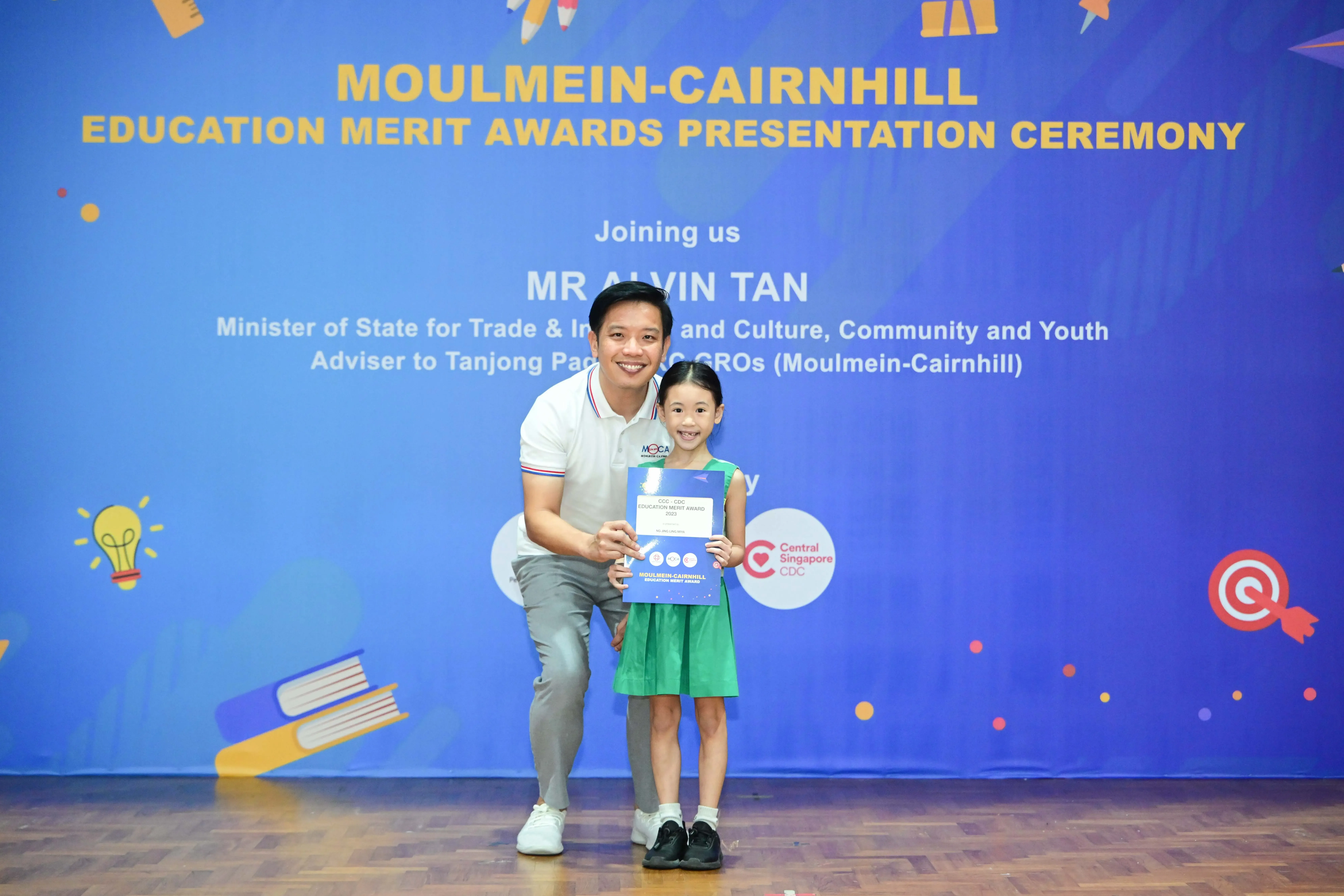 A man and a young girl hold a certificate at the Moulmein-Cairnhill Education Merit Awards Presentation Ceremony.