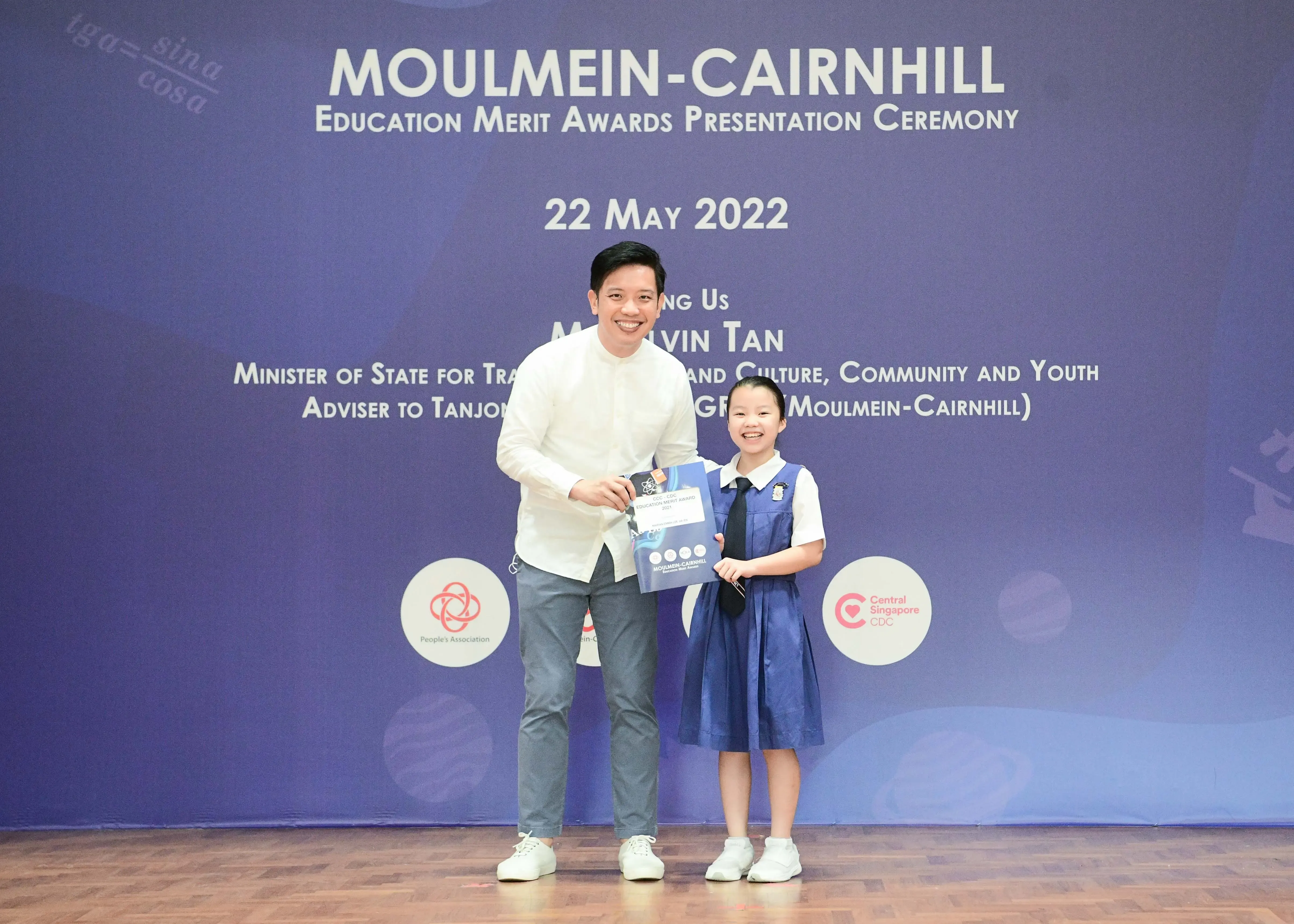A man and a young girl in school uniform smile holding an award booklet at the Moulmein-Cairnhill Education Merit Awards 2022.