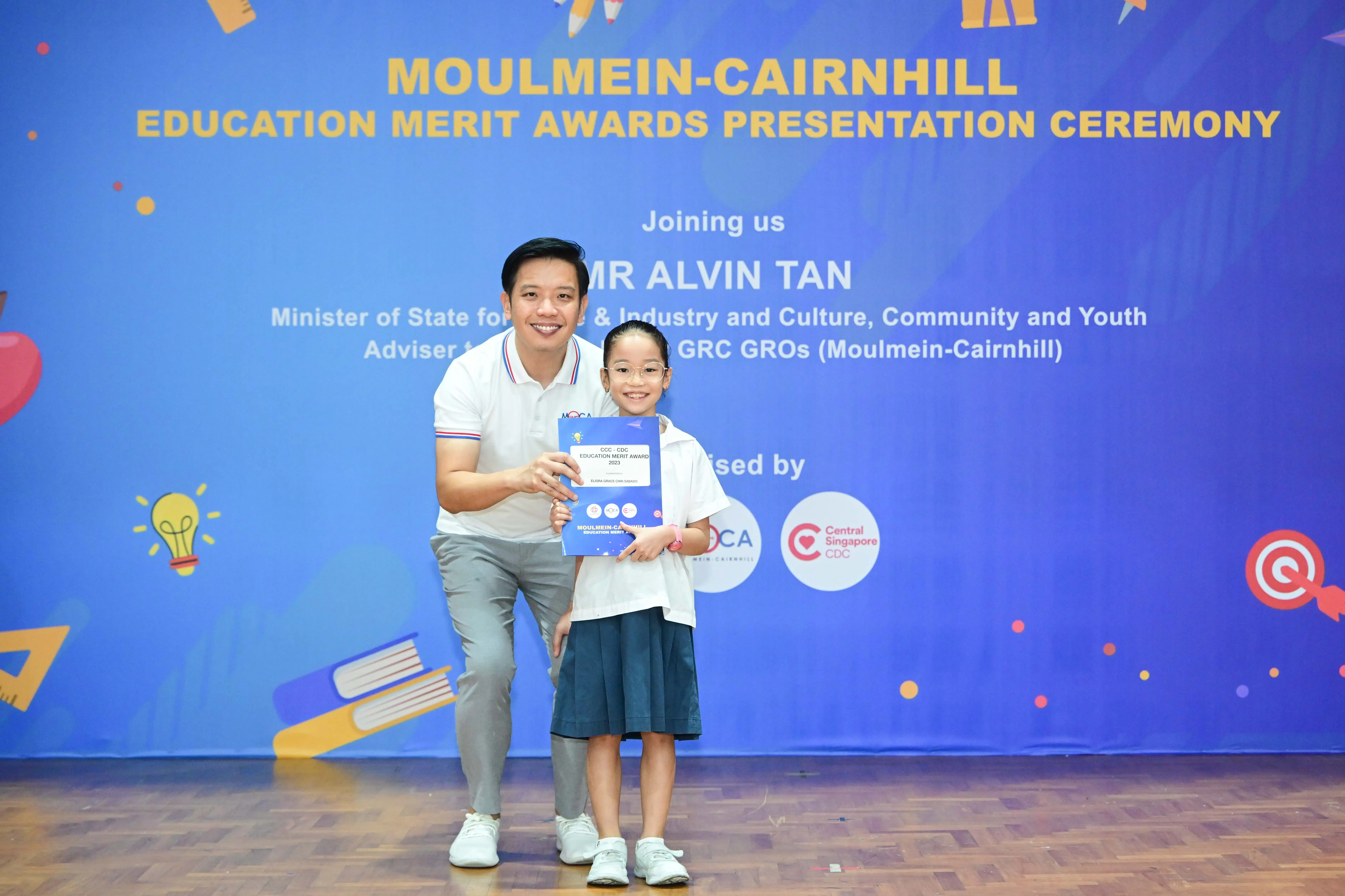 Man and young girl hold an award certificate at the Moulmein-Cairnhill Education Merit Awards Presentation Ceremony.