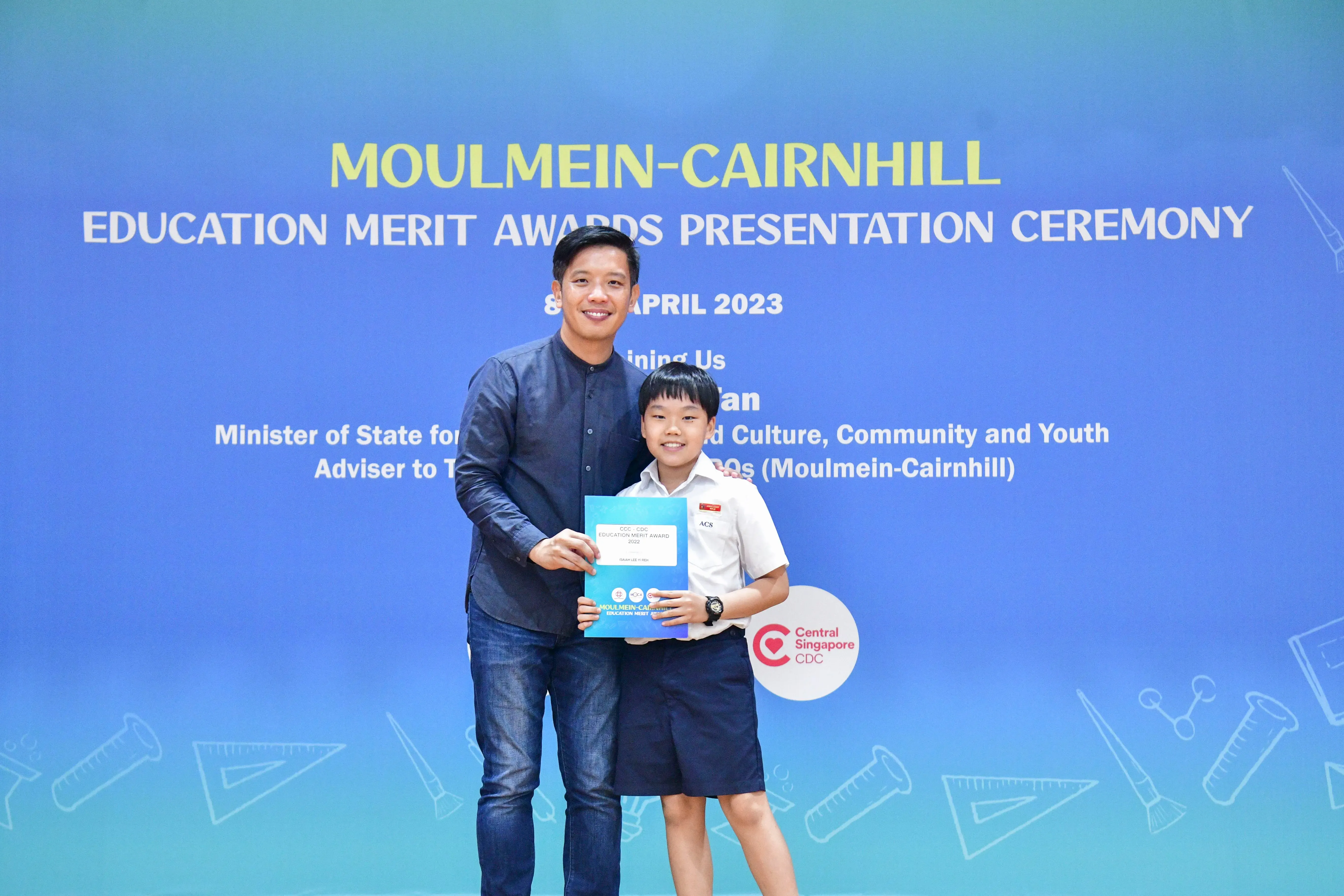 An adult and a young student pose together holding a certificate at the Moulmein-Cairnhill Education Merit Awards 2023.