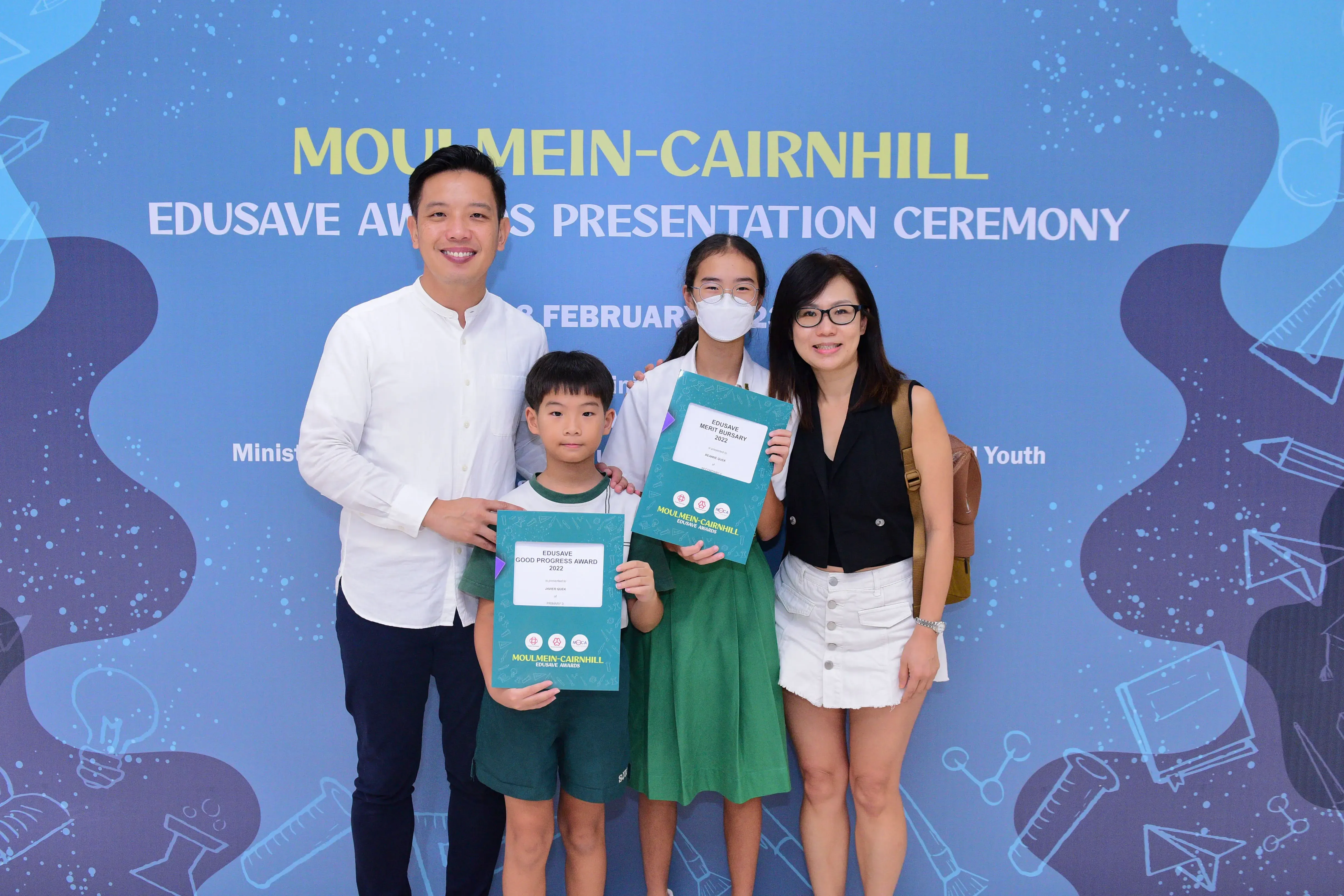 Four people pose with award certificates at the Moulmein-Cairnhill Edusave Awards Presentation Ceremony backdrop.