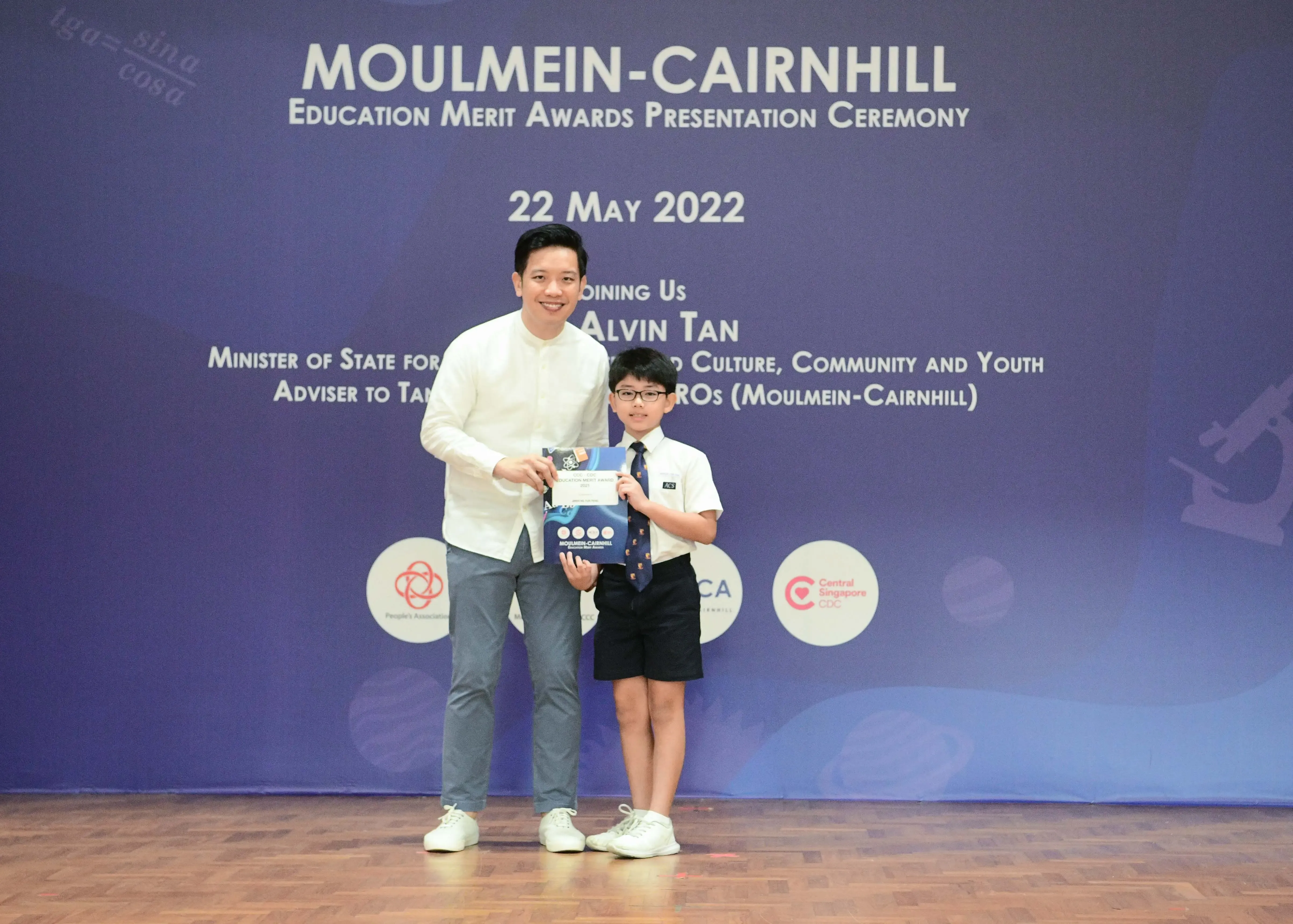 An adult and a young boy holding an award at the Moulmein-Cairnhill Education Merit Awards Ceremony on 22 May 2022.