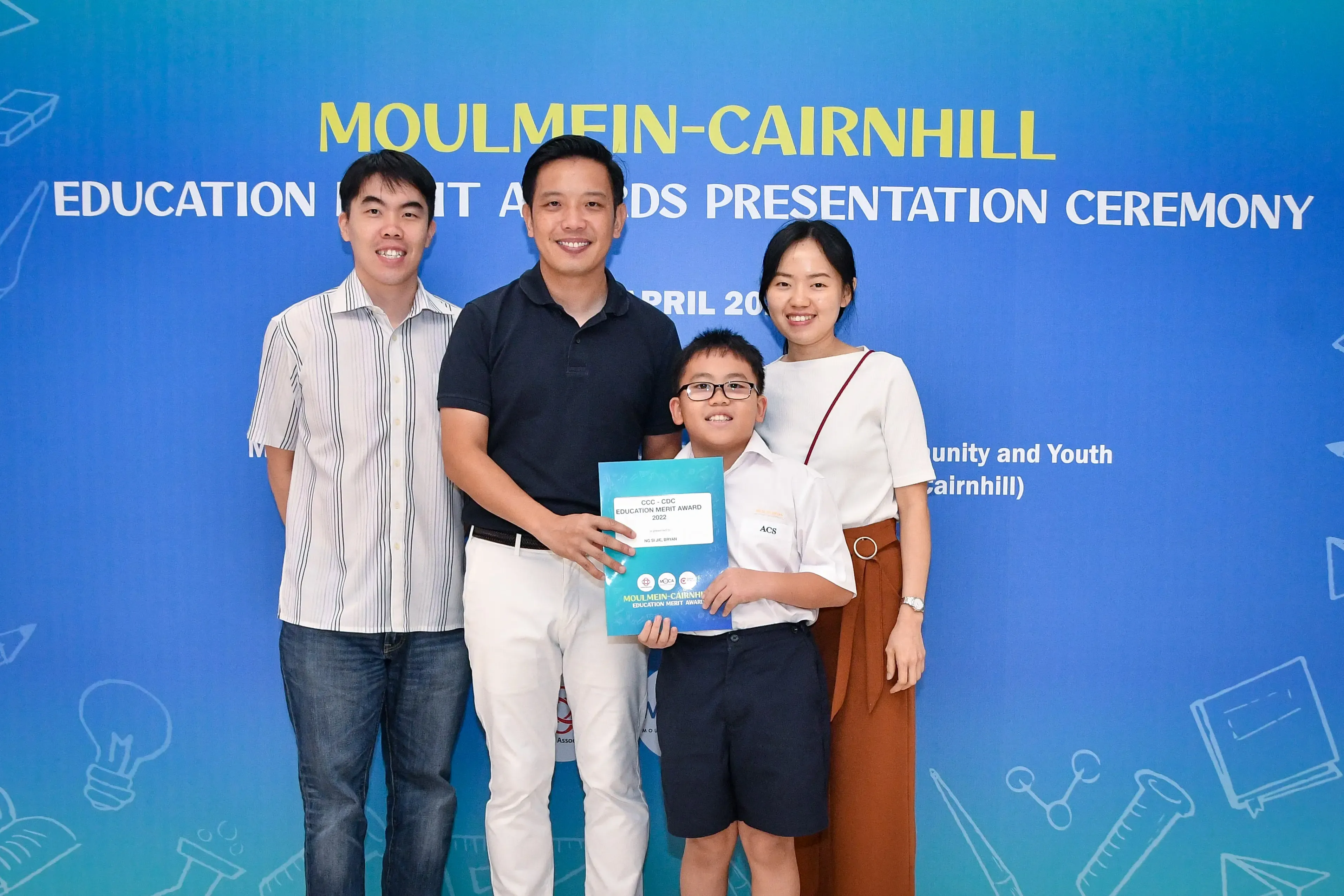 Four people smile holding an award certificate at the Moulmein-Cairnhill Education Merit Awards Presentation Ceremony.