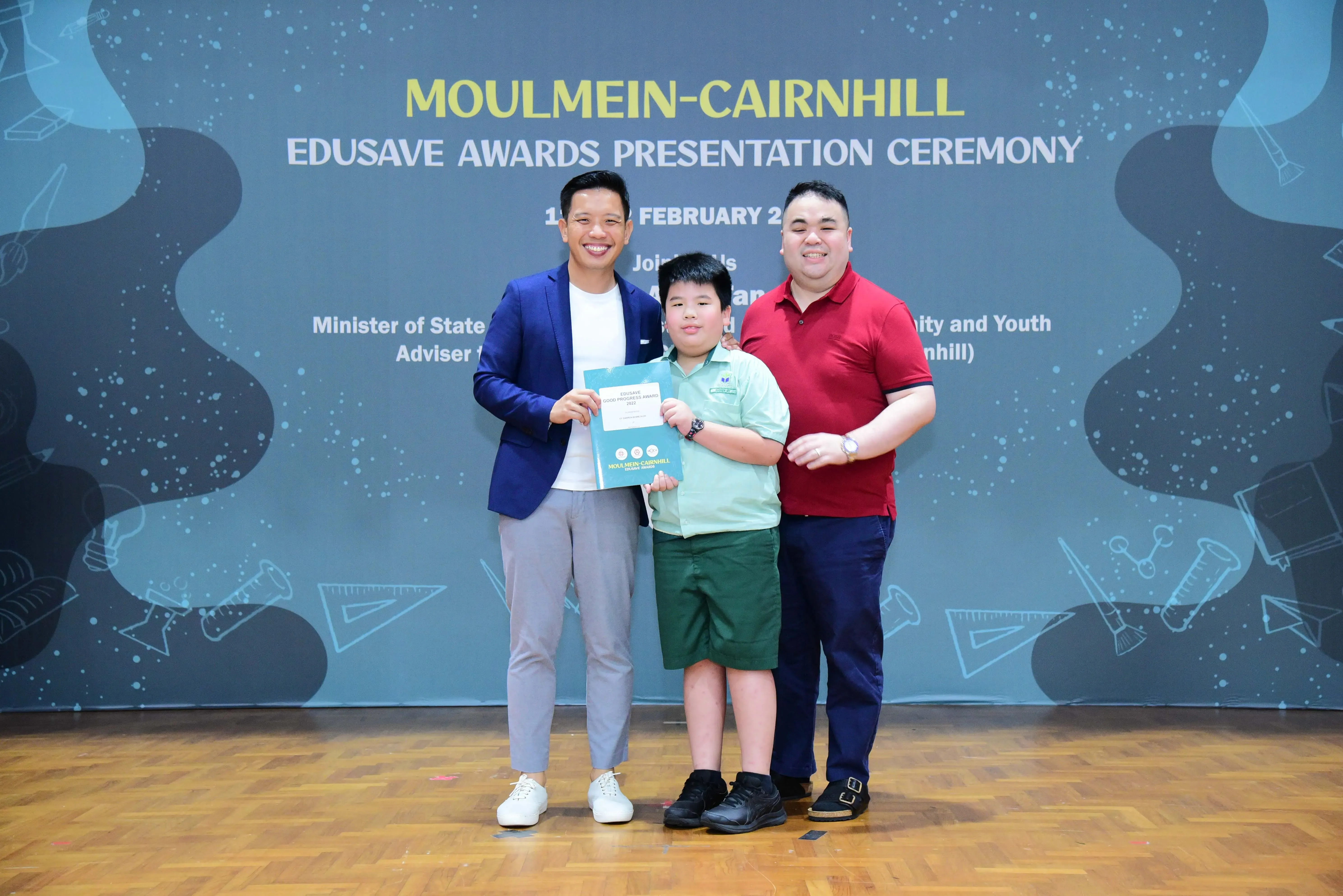 Two adults and a young student holding a certificate pose at the Moulmein-Cairnhill Edusave Awards Presentation Ceremony.