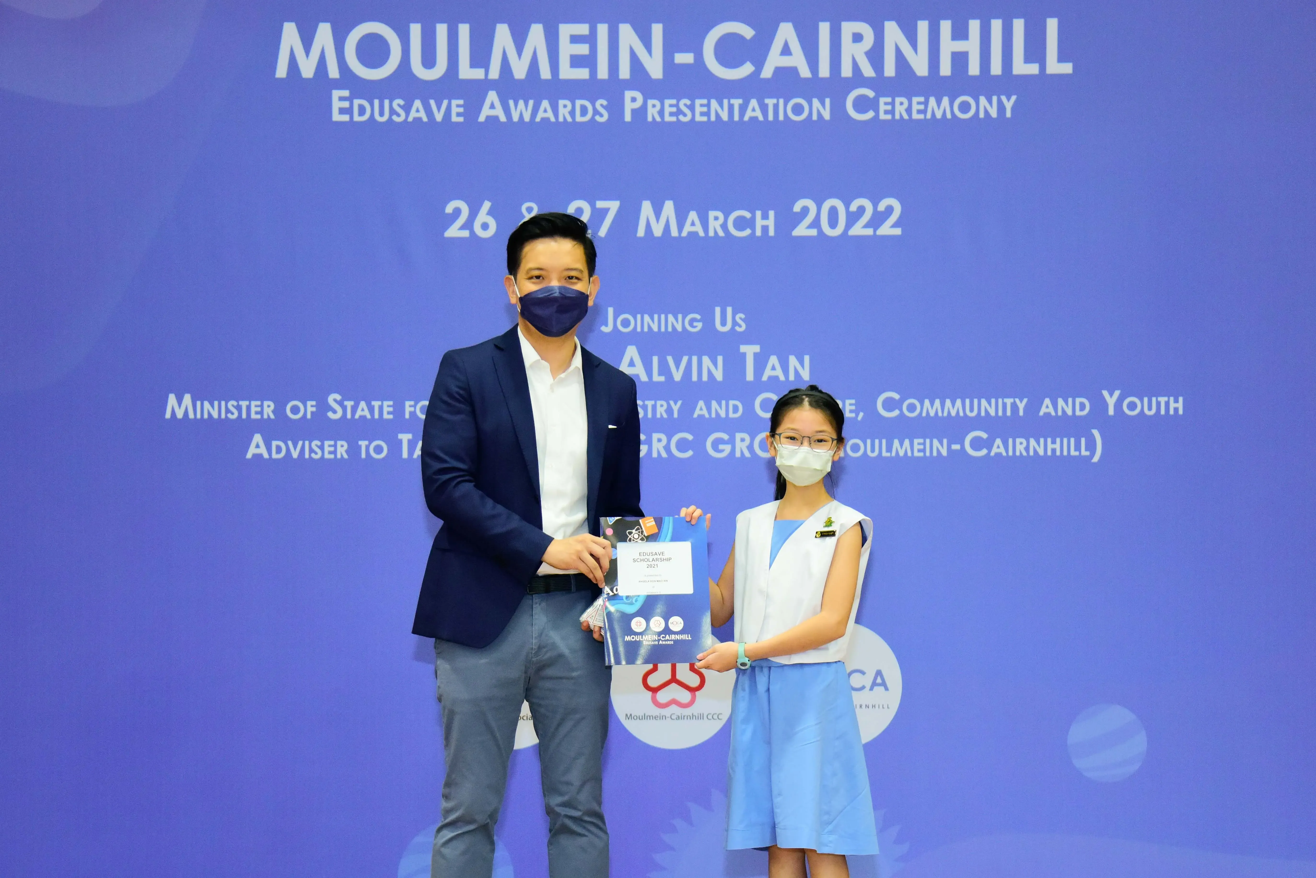 A man and a young girl wearing masks hold an award certificate at the Moulmein-Cairnhill Edusave Awards Ceremony 2022.