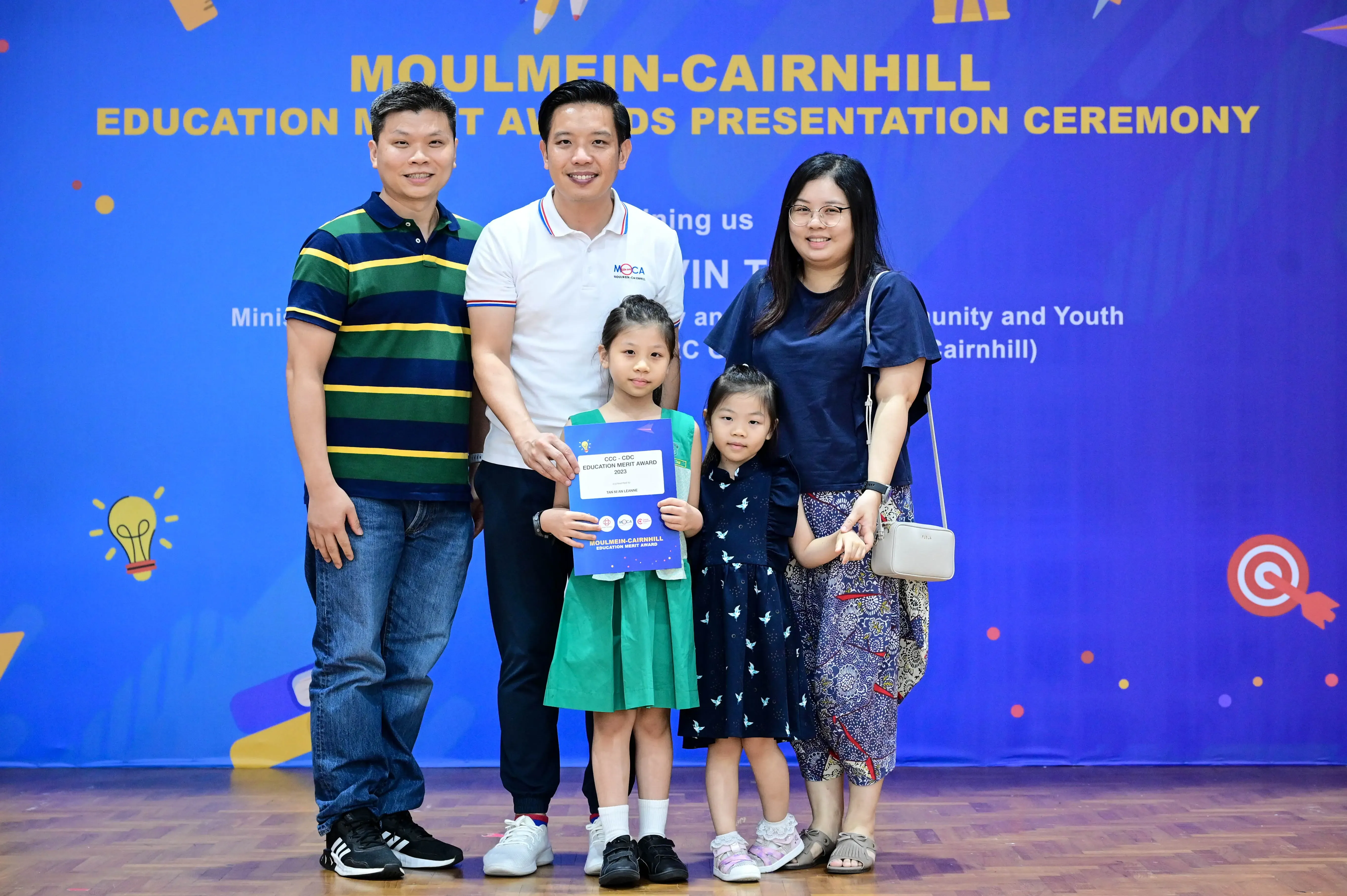 Five people including two young girls pose with a certificate at the Moulmein-Cairnhill Education Merit Awards ceremony.