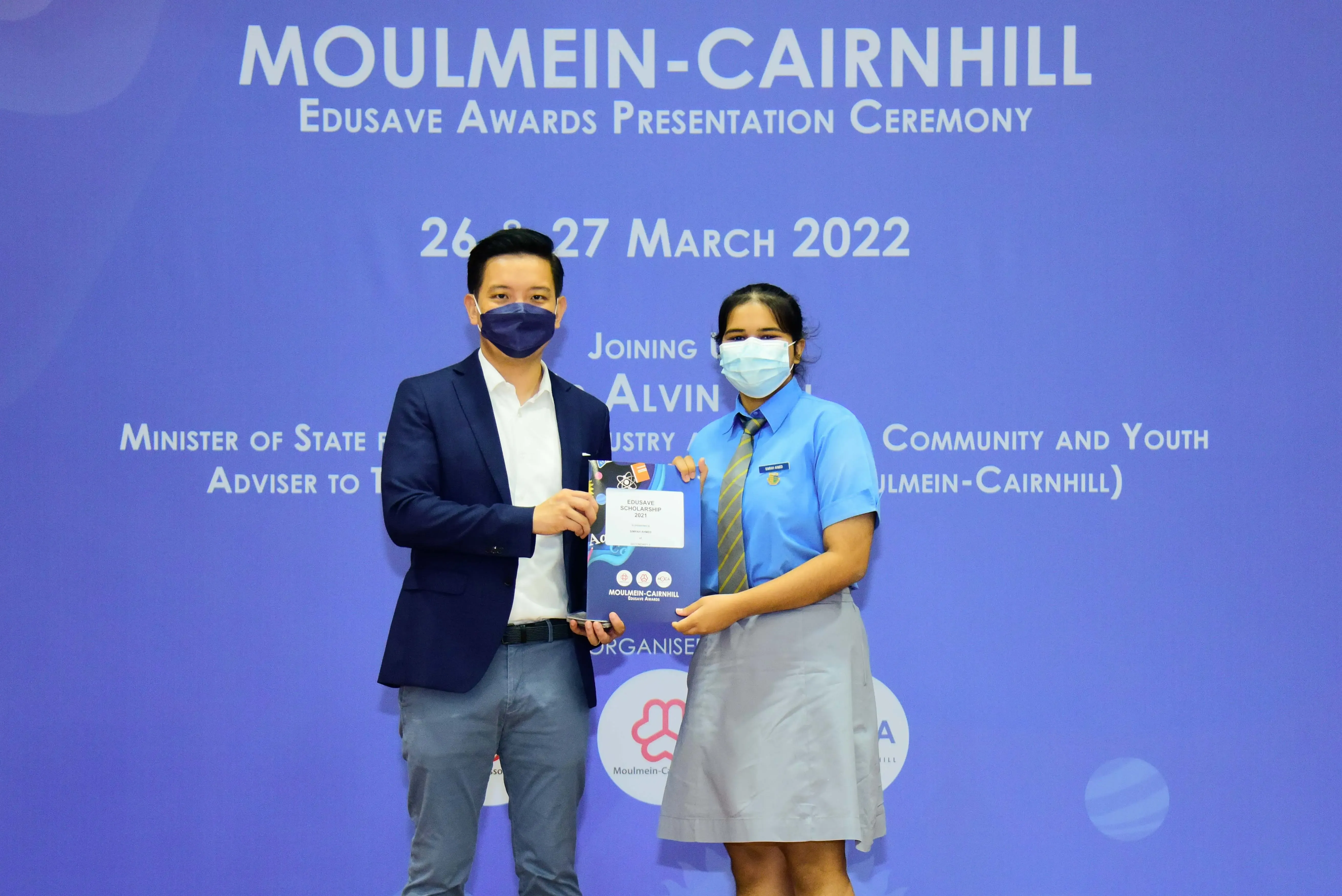Two masked people hold an award folder at the Moulmein-Cairnhill Edusave Awards Ceremony on March 26-27, 2022.