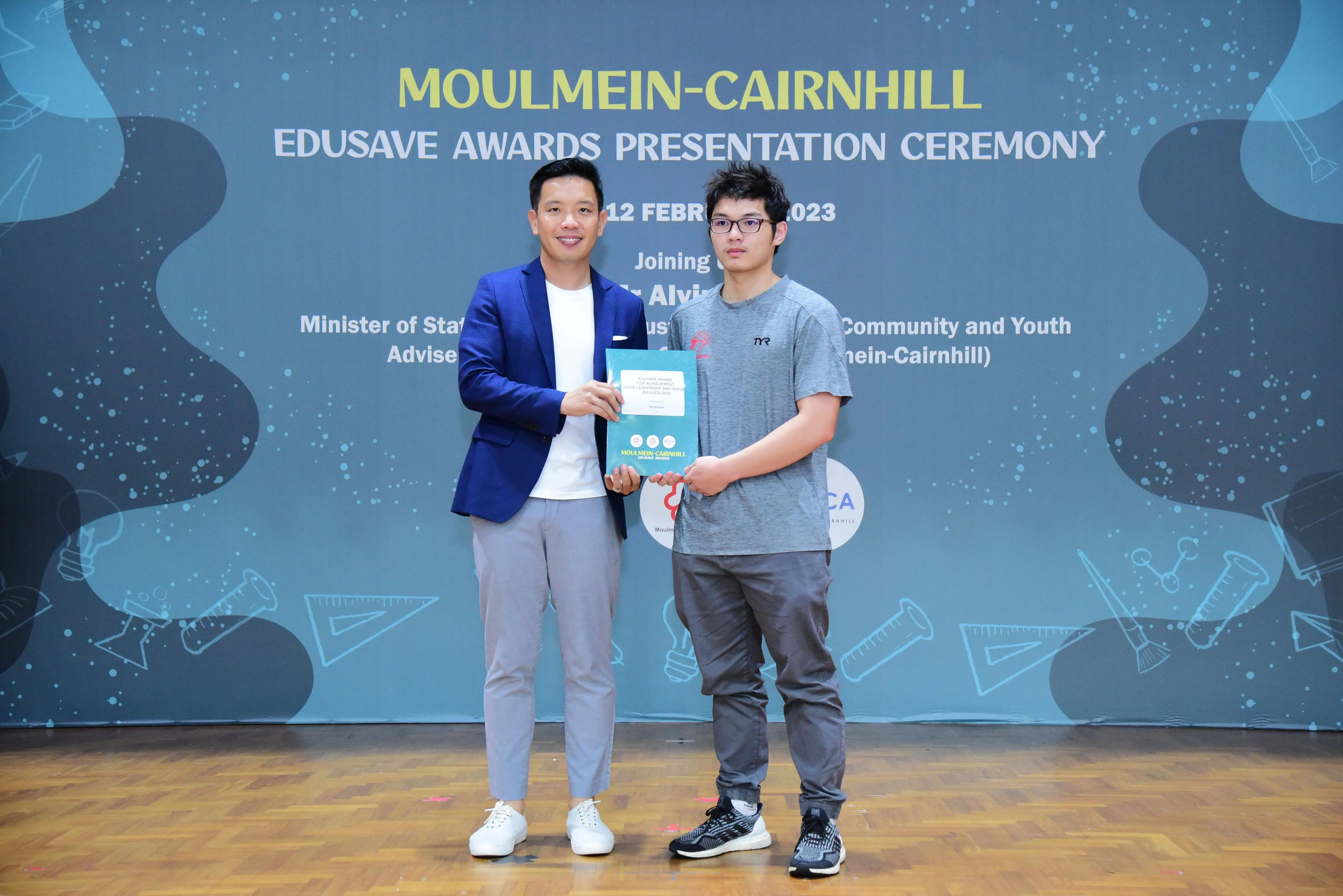 Two men hold a certificate together at the Moulmein-Cairnhill Edusave Awards Presentation Ceremony 2023.