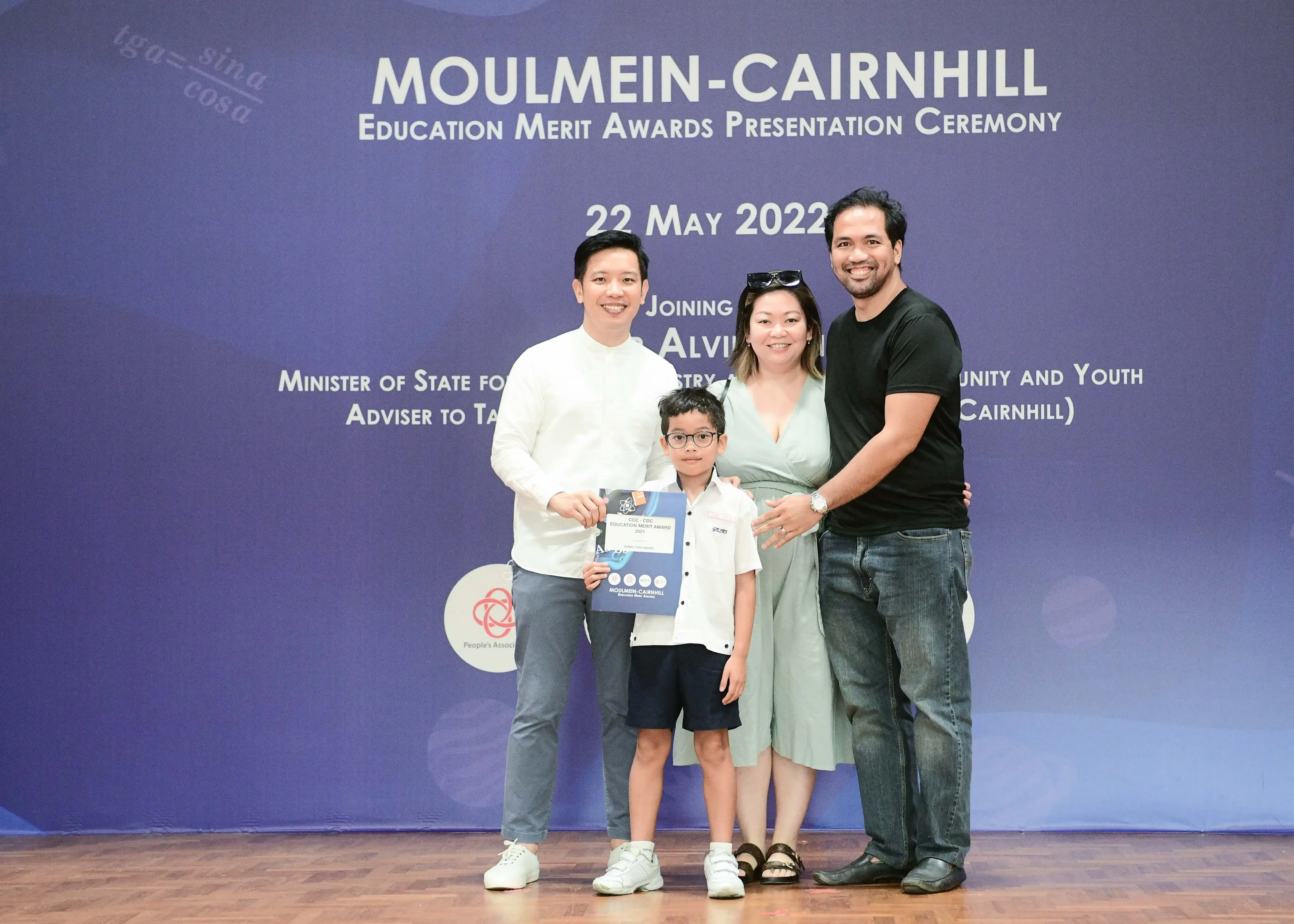 Four people posing at the Moulmein-Cairnhill Education Merit Awards Ceremony on 22 May 2022, with a boy holding a certificate.