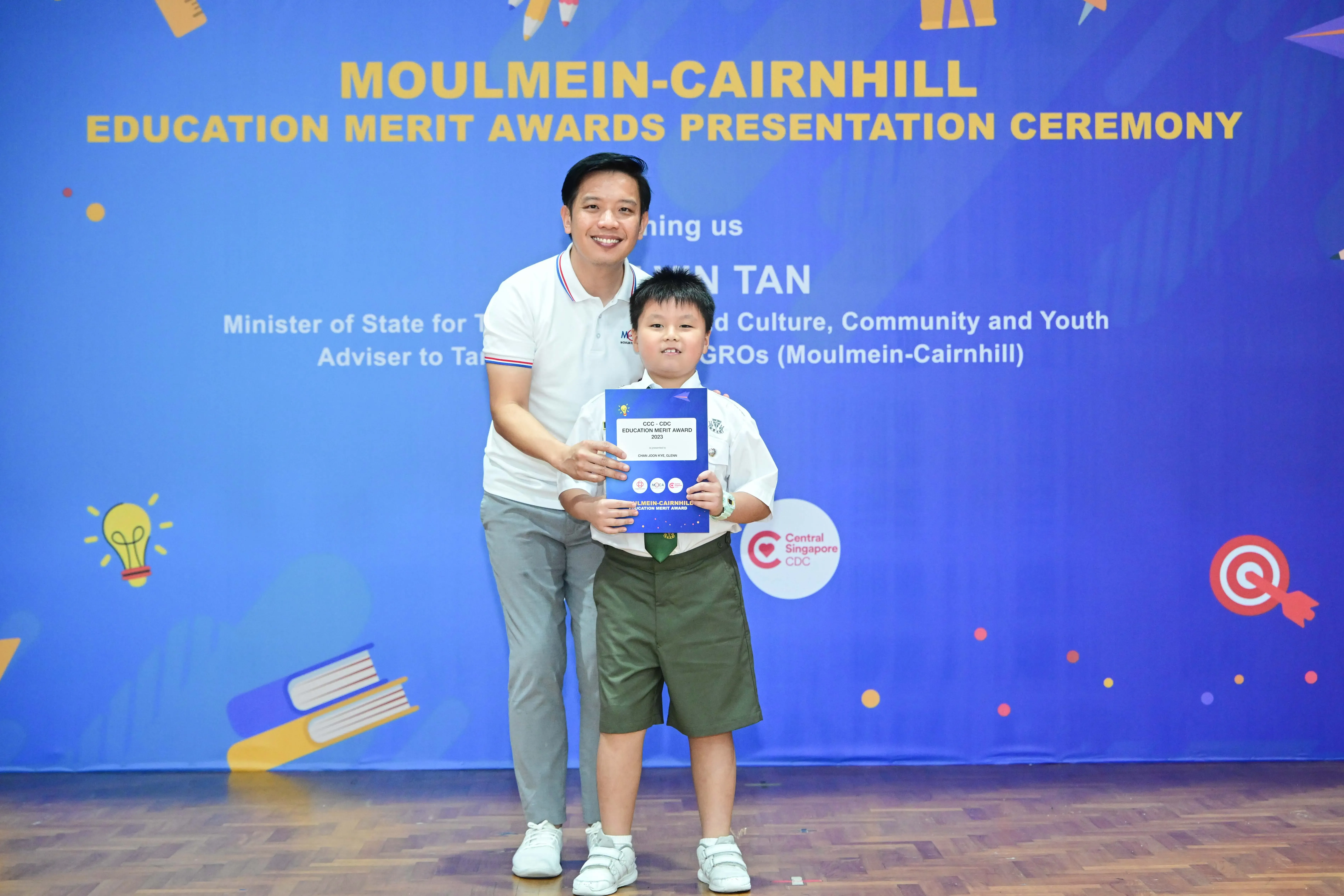 A man and young boy pose together holding an award certificate at the Moulmein-Cairnhill Education Merit Awards ceremony.