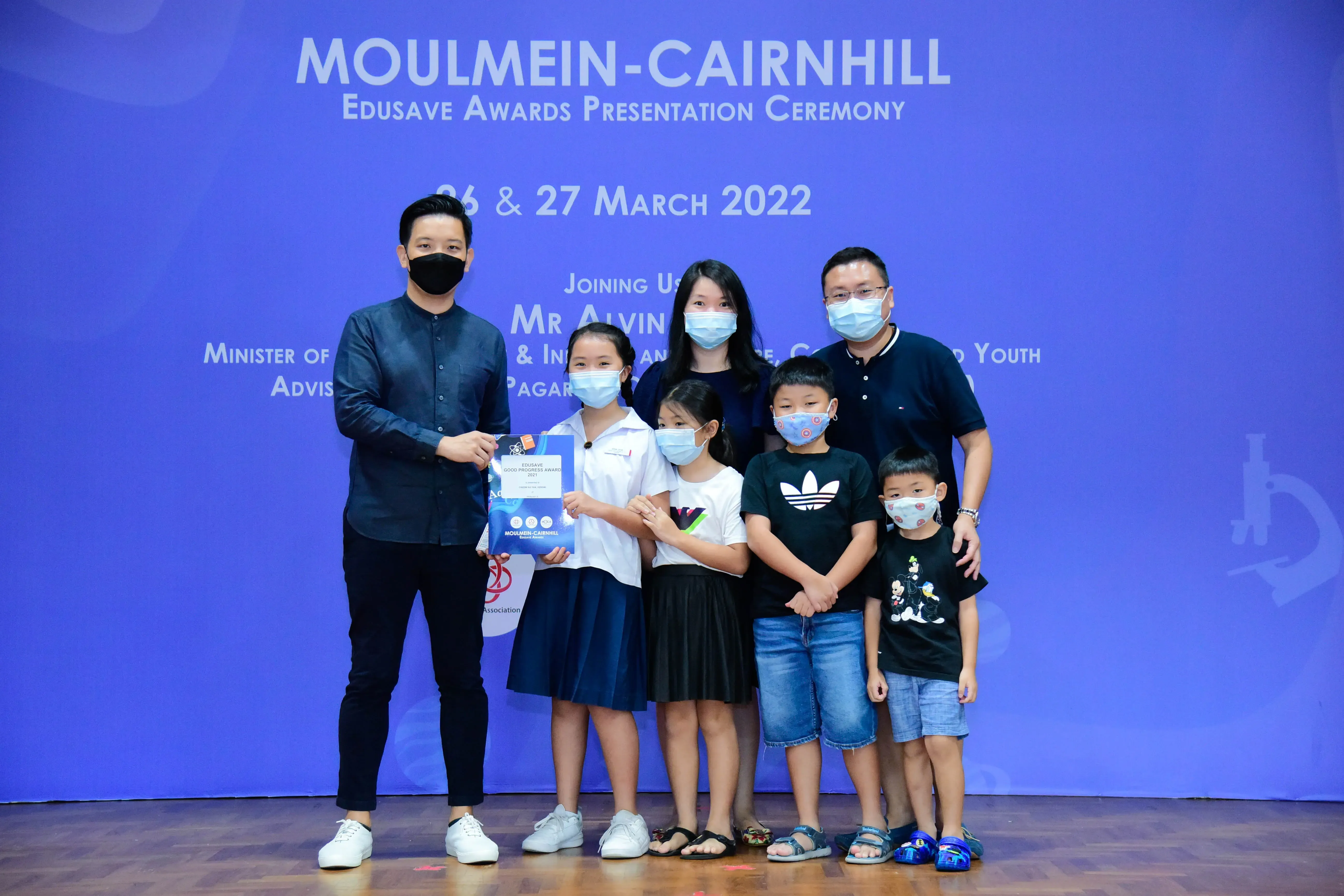 Adults and children wearing masks pose at the Moulmein-Cairnhill Edusave Awards Presentation Ceremony, March 2022.