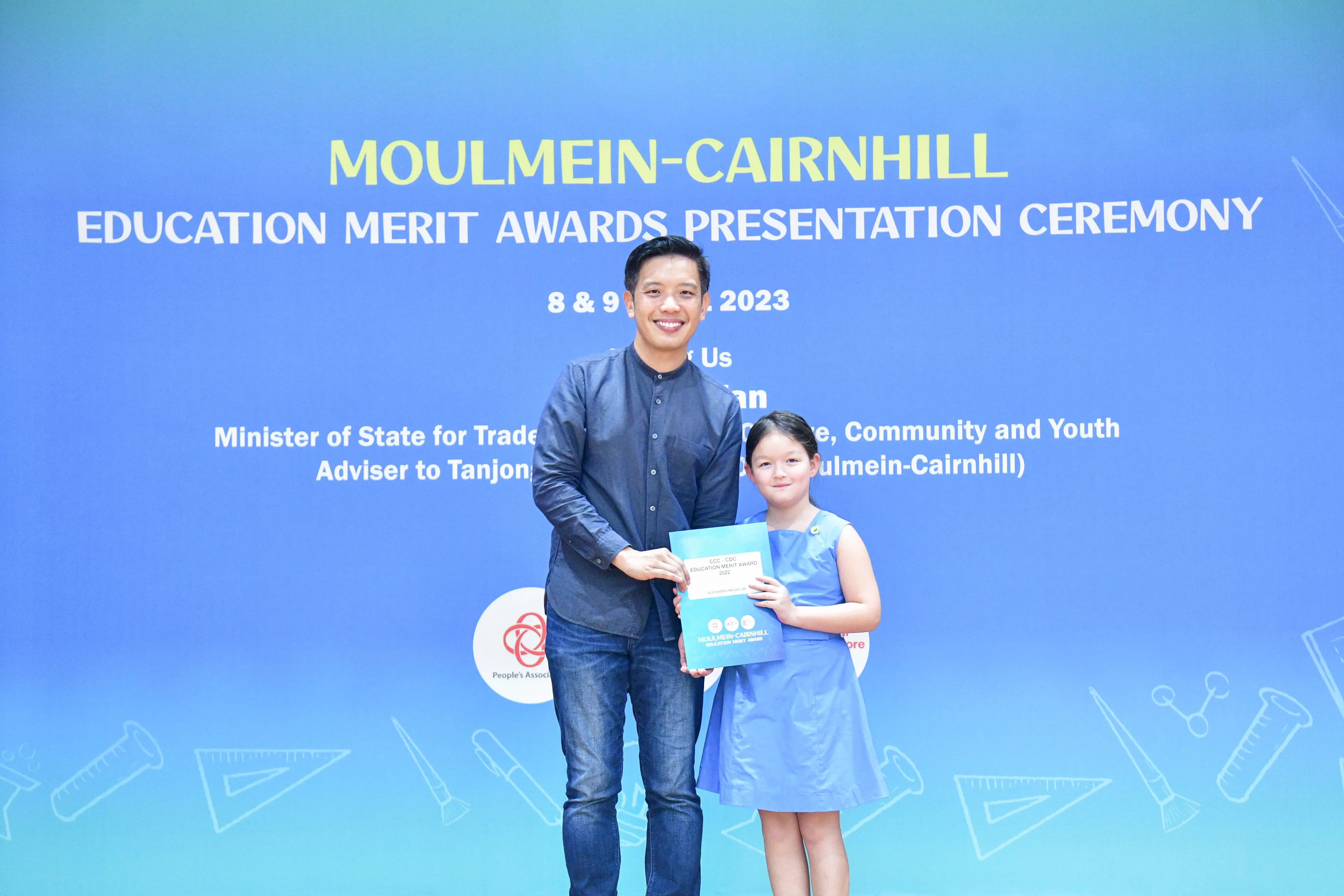 A man and a young girl hold an award certificate at the Moulmein-Cairnhill Education Merit Awards Ceremony 2023.