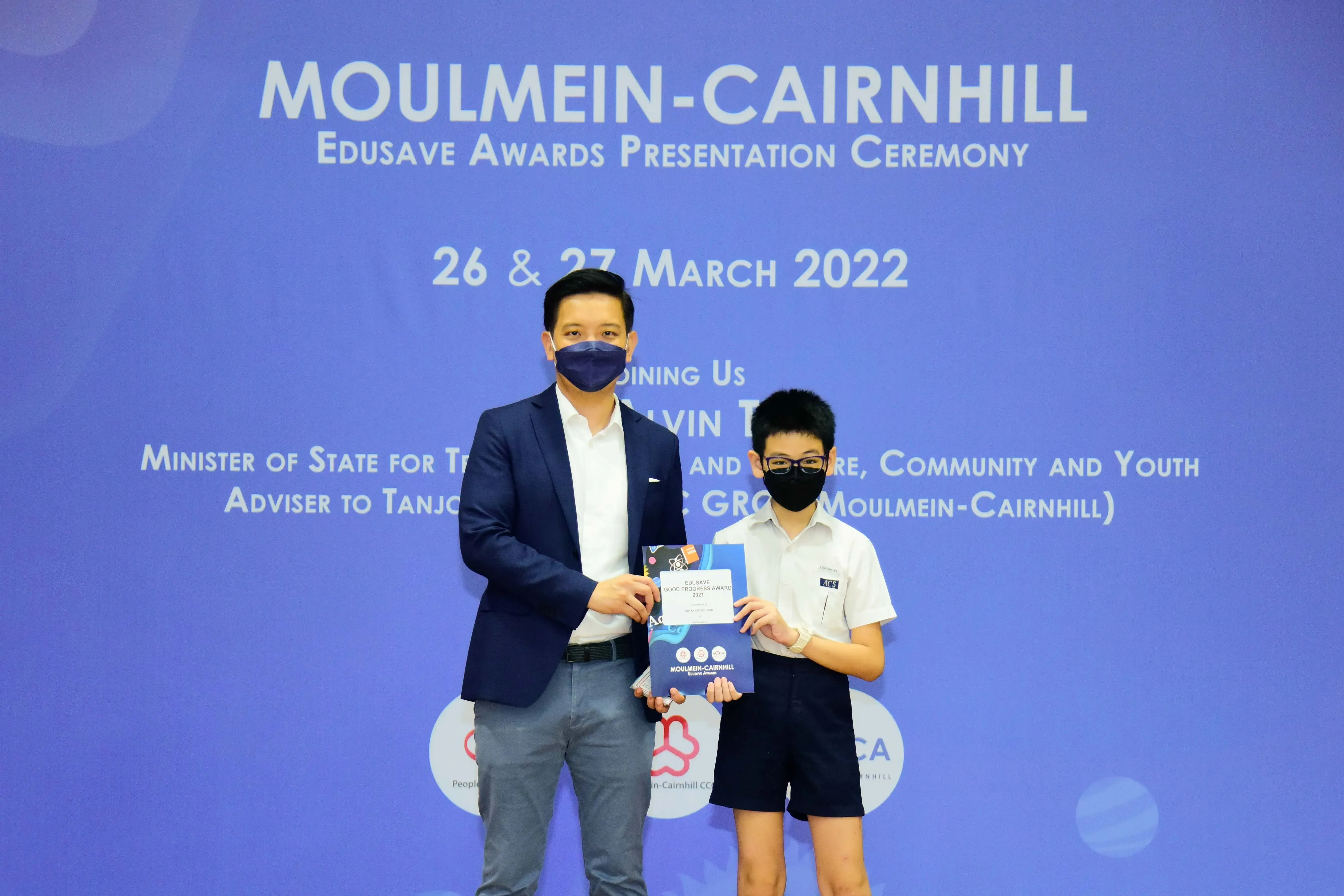 An adult and a young student in masks hold an award booklet at the Moulmein-Cairnhill Edusave Awards Ceremony, March 2022.