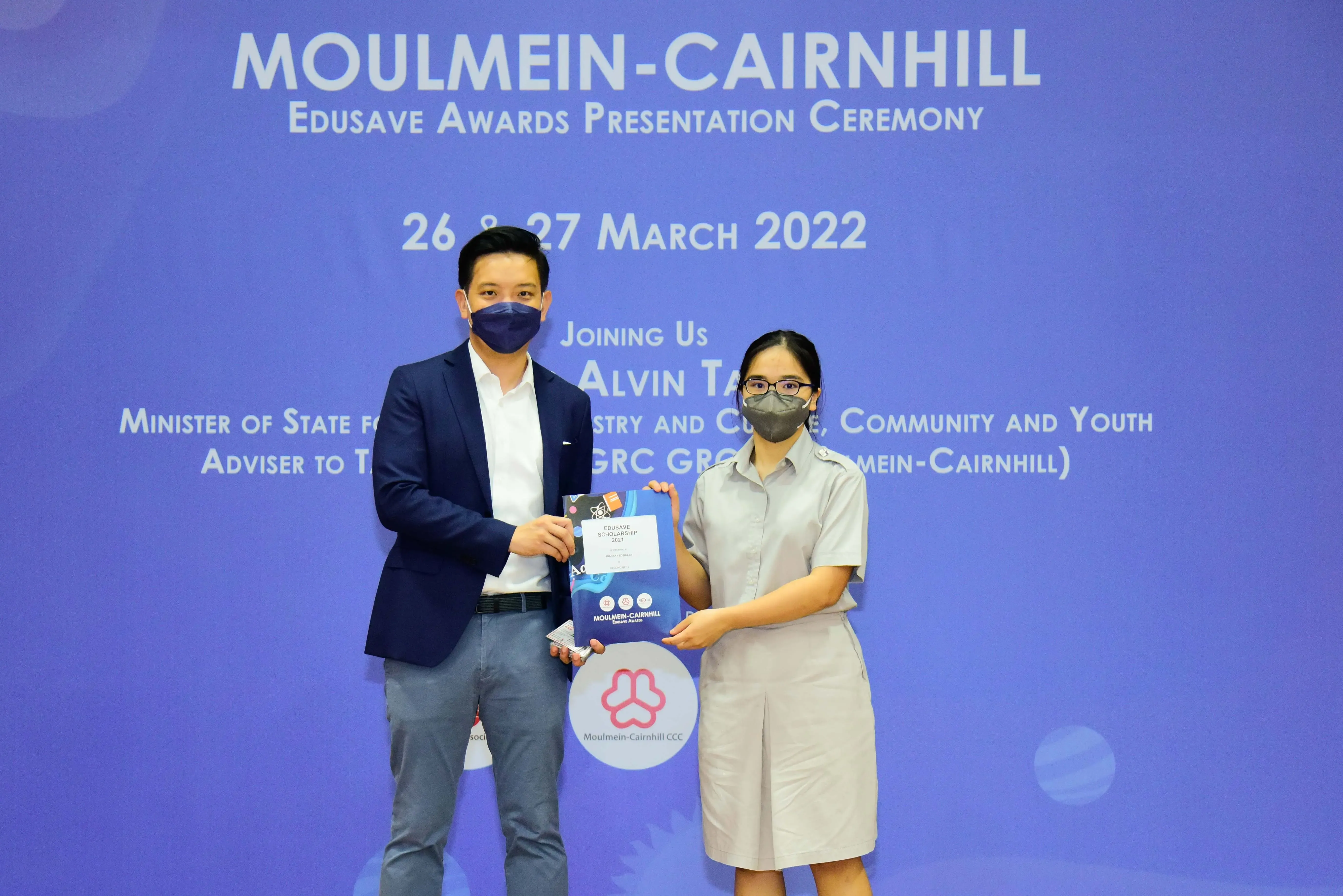 Two masked people hold an award booklet at the Moulmein-Cairnhill Edusave Awards Ceremony, March 2022.