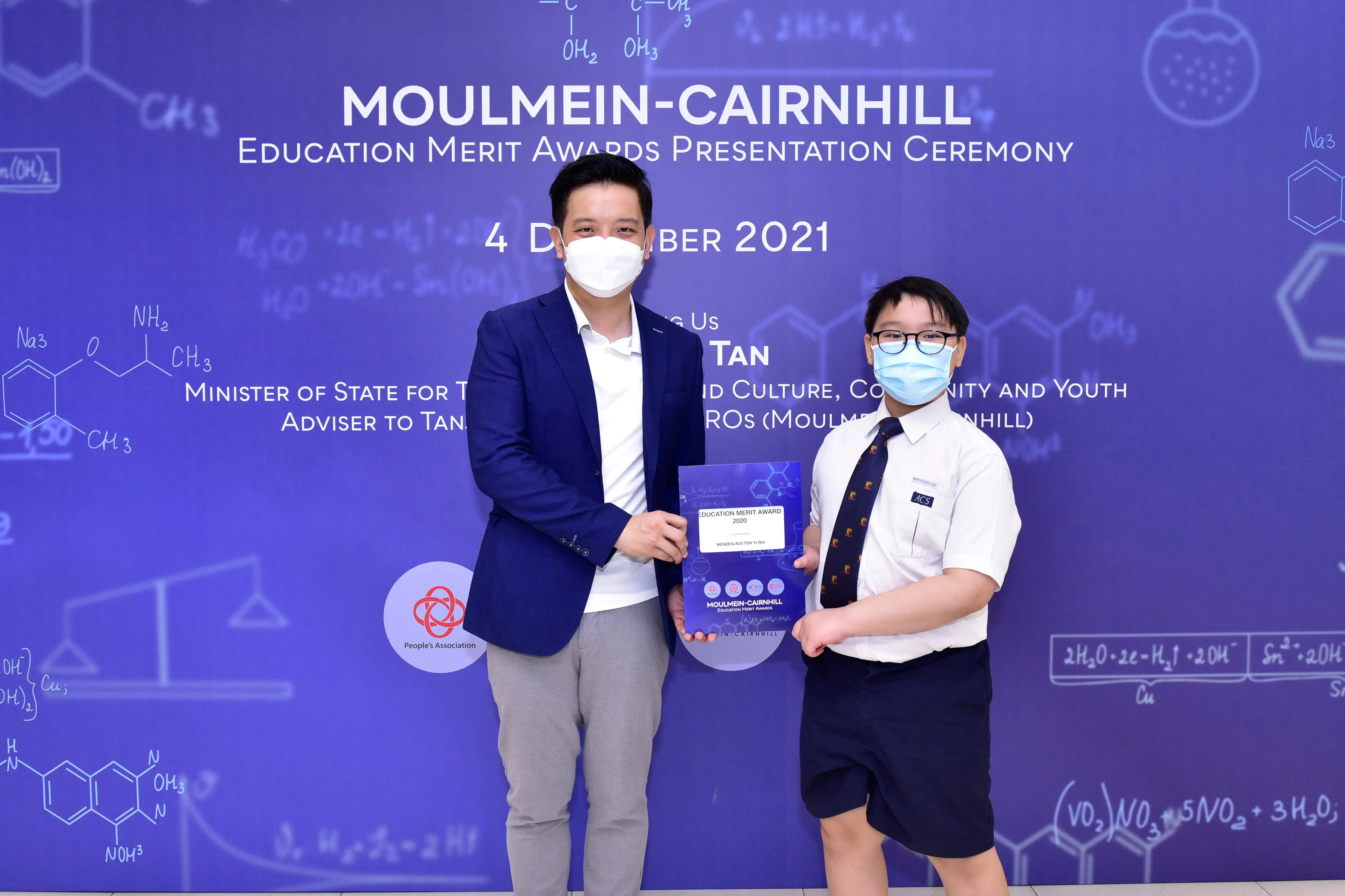 Two masked individuals hold an award certificate at the Moulmein-Cairnhill Education Merit Awards Ceremony, 4 December 2021.