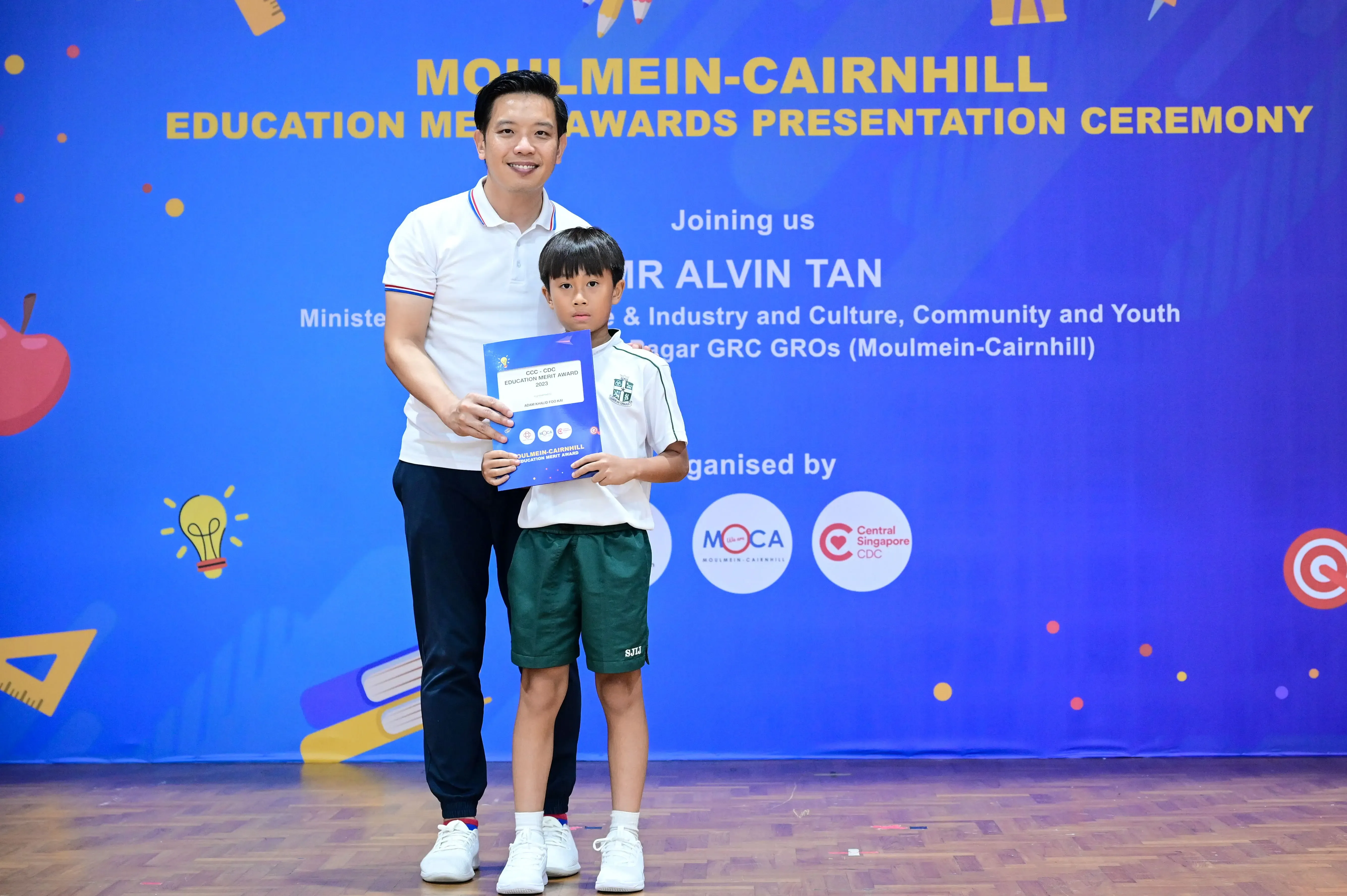 A man and a young boy hold a certificate at the Moulmein-Cairnhill Education Merit Awards Presentation Ceremony.
