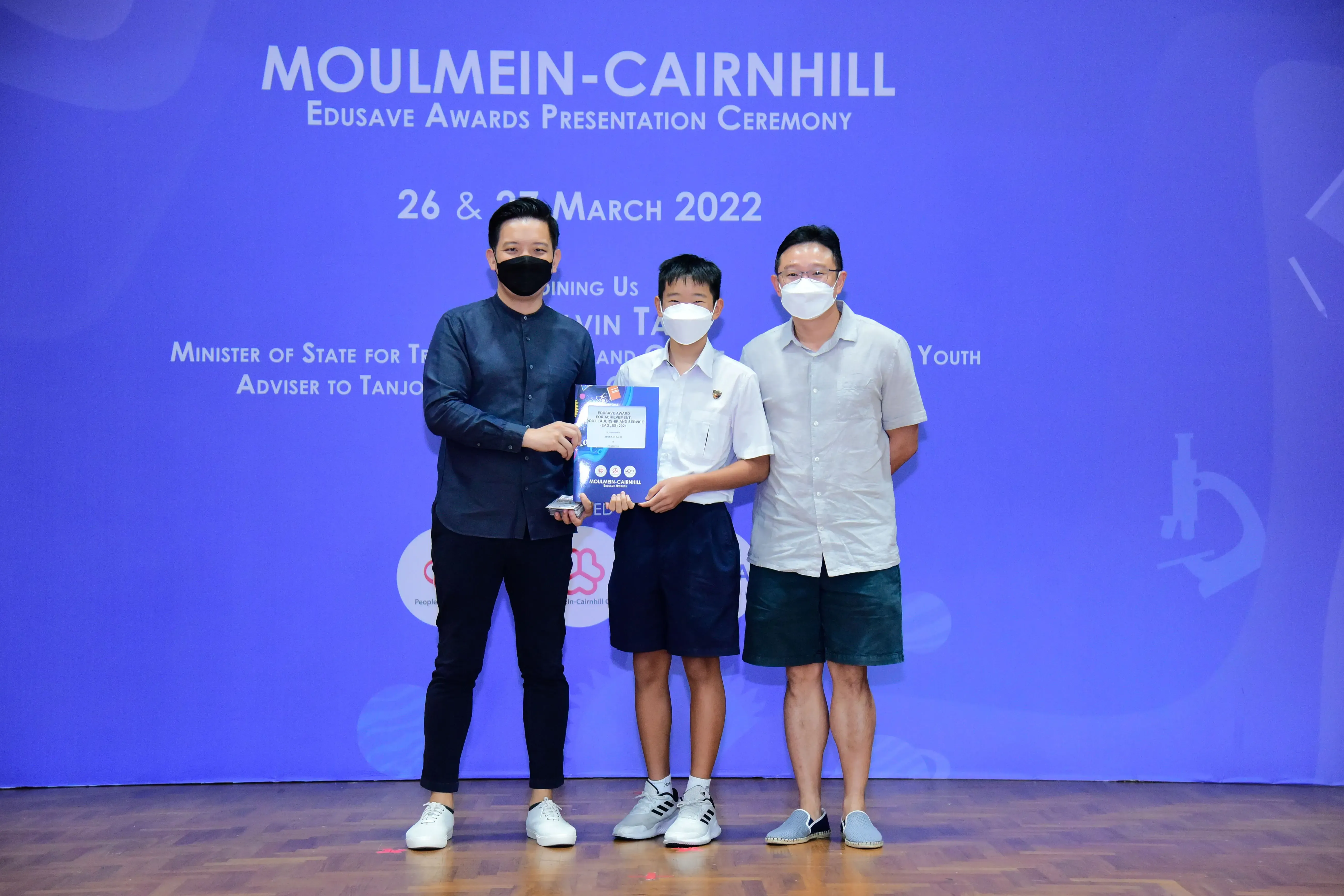 Three masked individuals pose on stage at the Moulmein-Cairnhill Edusave Awards Ceremony on 26 & 27 March 2022.