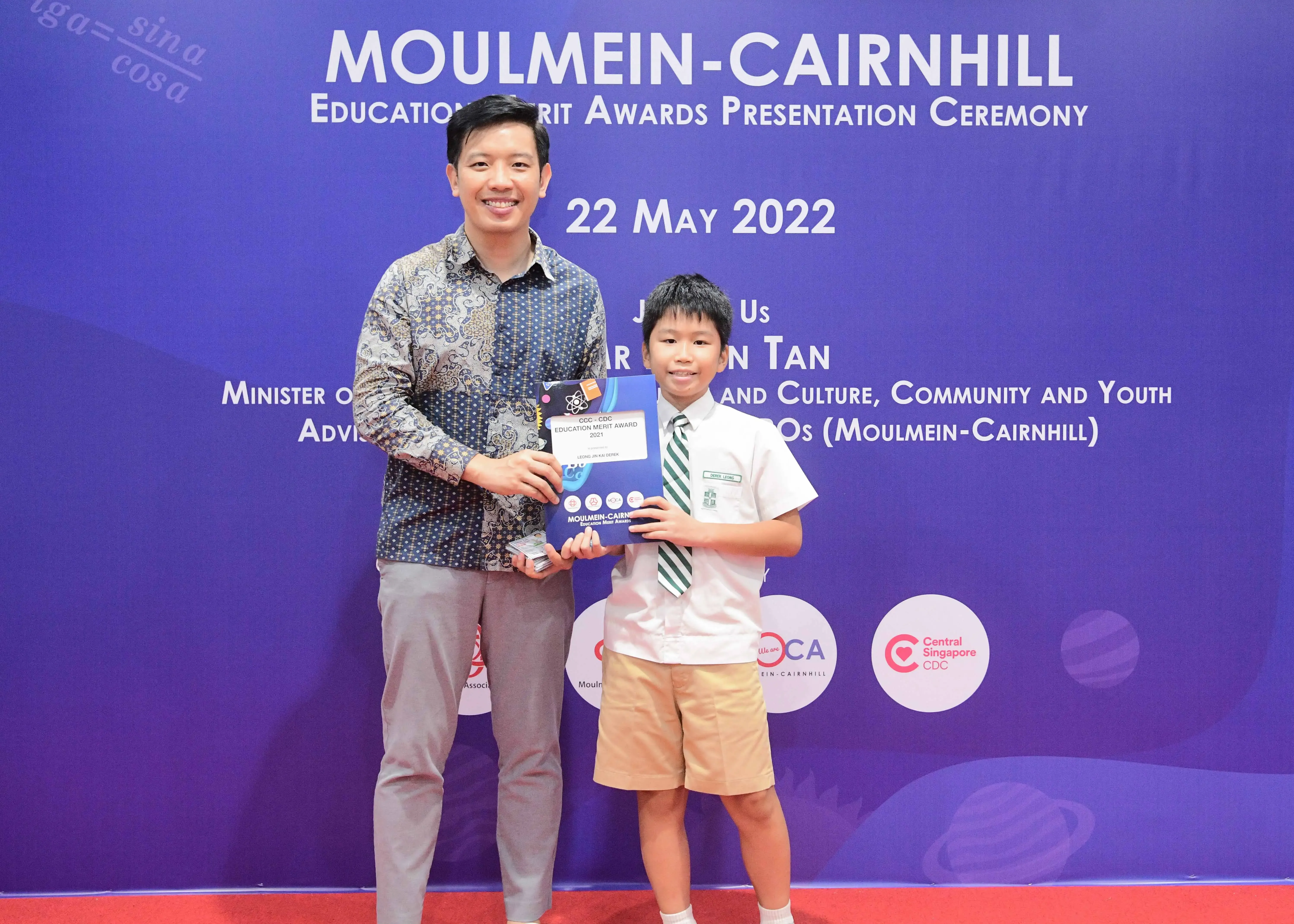 A man and a young boy in school uniform hold an award at the Moulmein-Cairnhill Education Merit Awards ceremony on 22 May 2022.