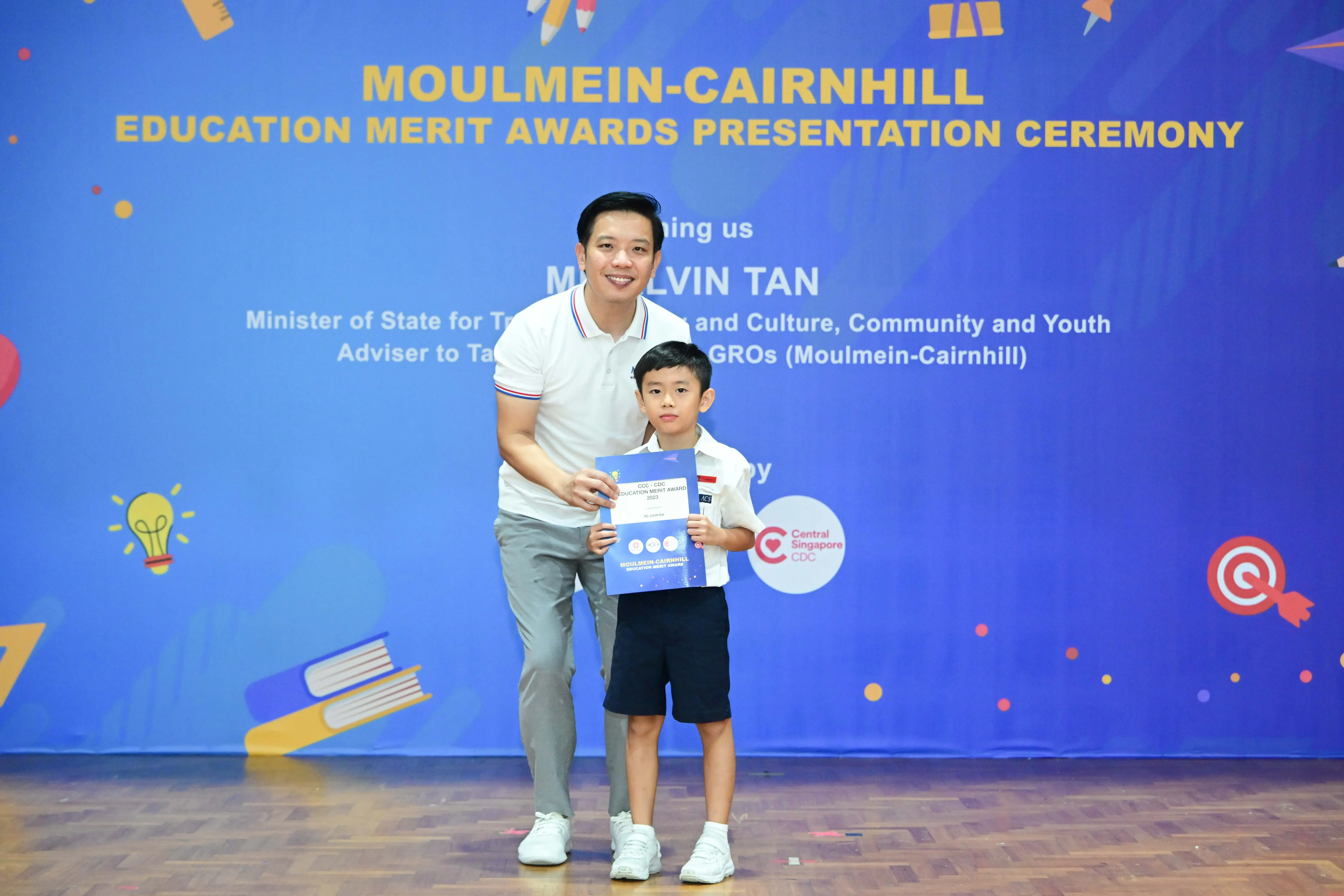 A man and young boy hold a certificate at the Moulmein-Cairnhill Education Merit Awards Presentation Ceremony.