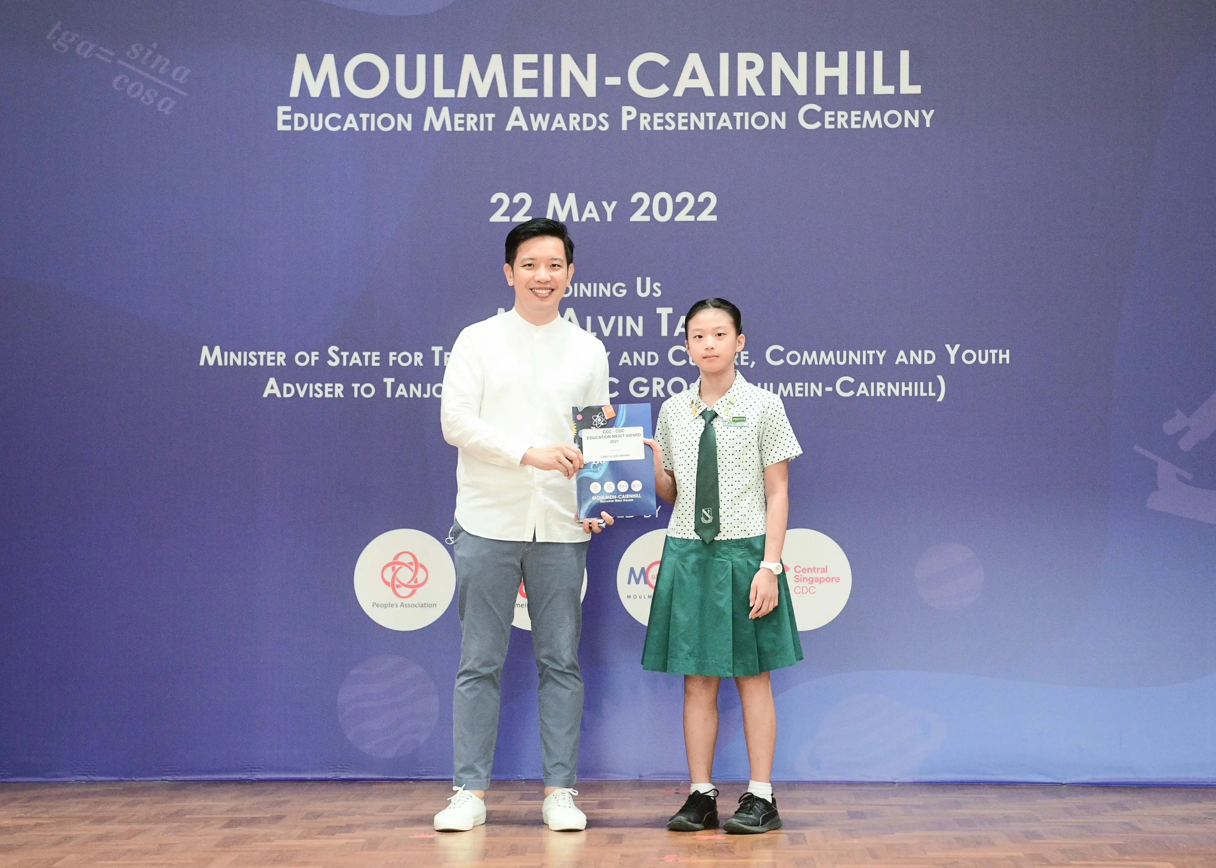 A man and a young girl in school uniform hold an award at the Moulmein-Cairnhill Education Merit Awards ceremony on 22 May 2022.