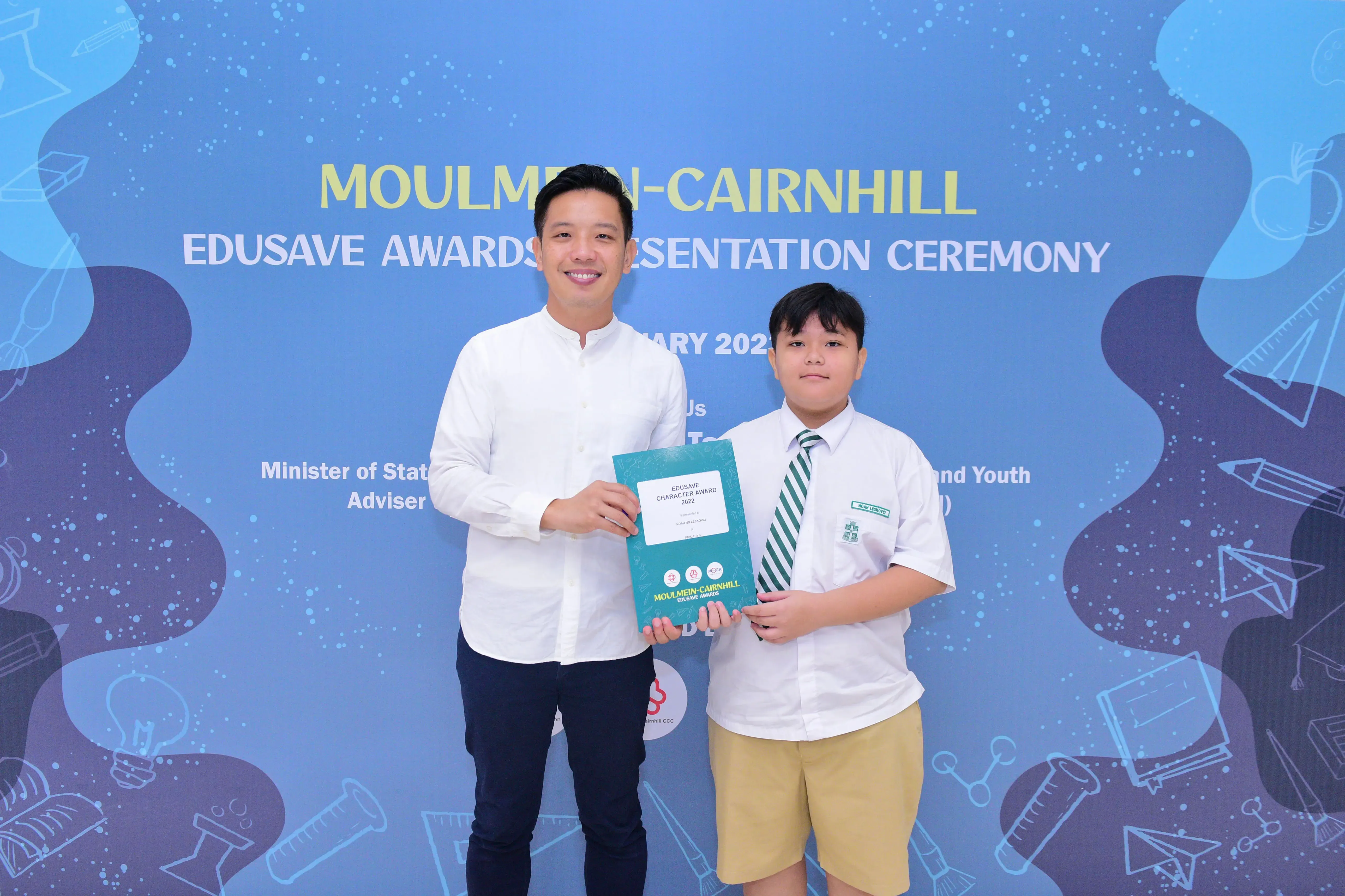 Man in white shirt and young student in uniform hold an award certificate at Moulmein-Cairnhill Edusave Awards Ceremony.