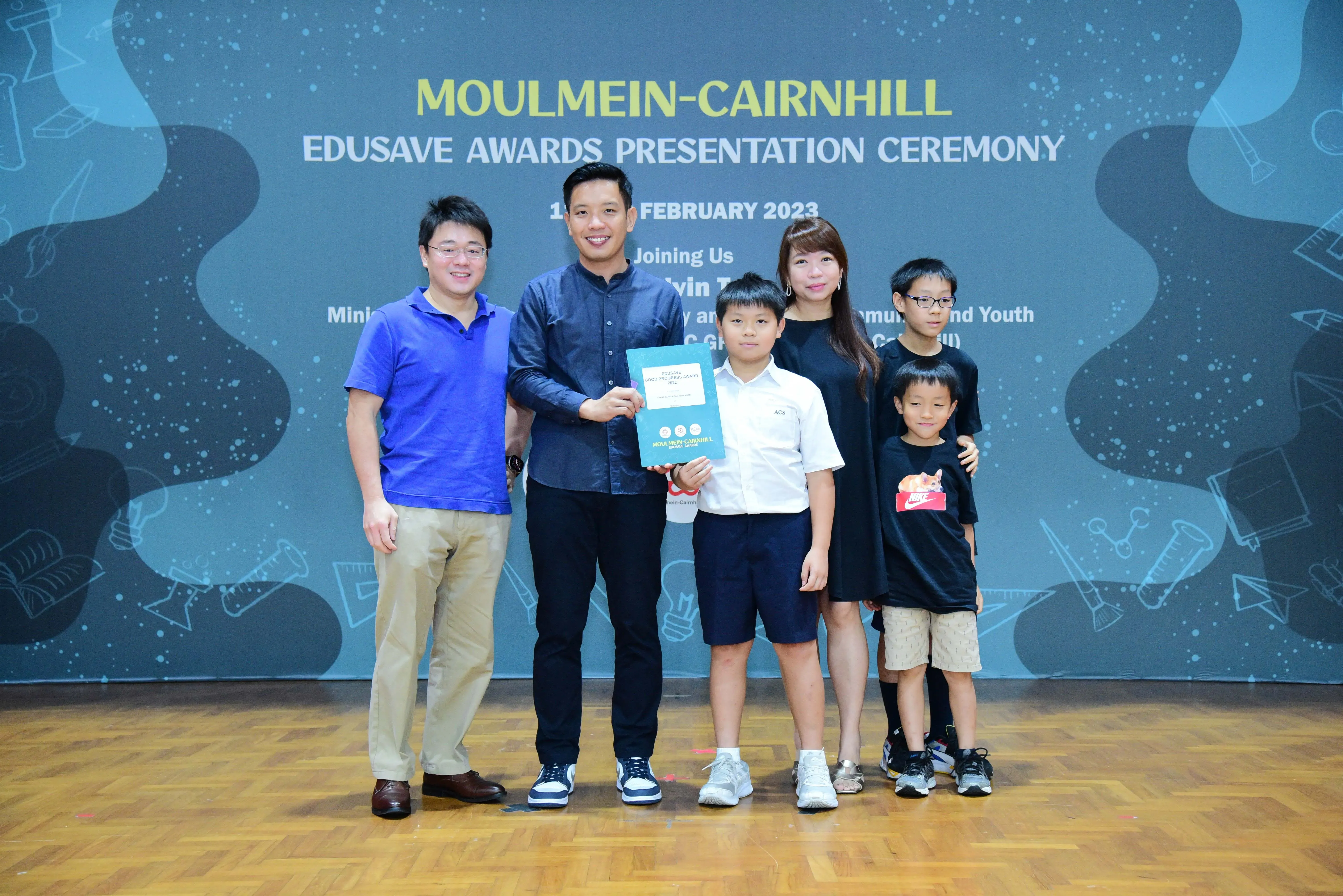 Six people pose at the Moulmein-Cairnhill Edusave Awards Presentation Ceremony in February 2023, with a boy holding a certificate.