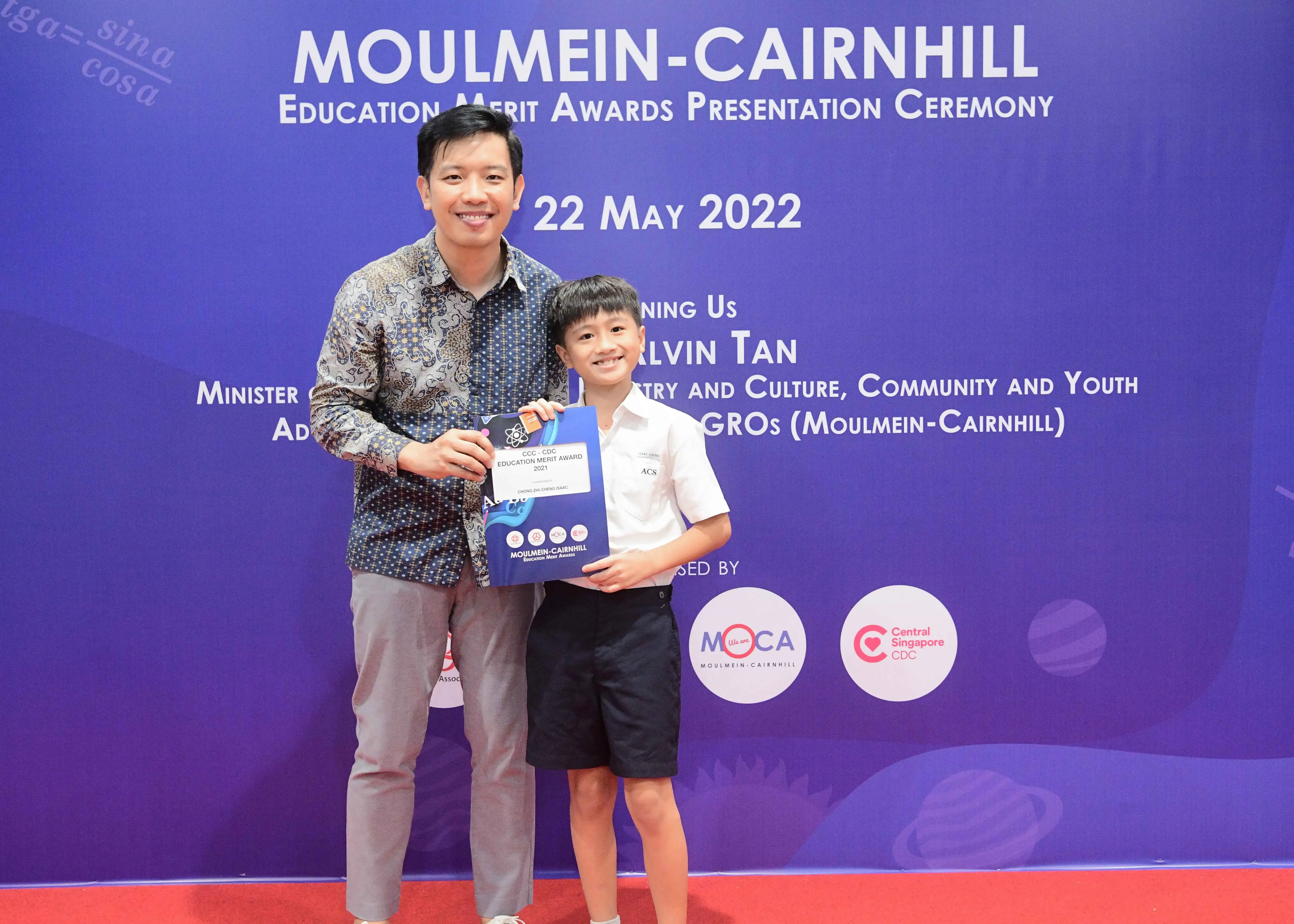 Man and young boy pose holding an award folder at the Moulmein-Cairnhill Education Merit Awards ceremony on 22 May 2022.