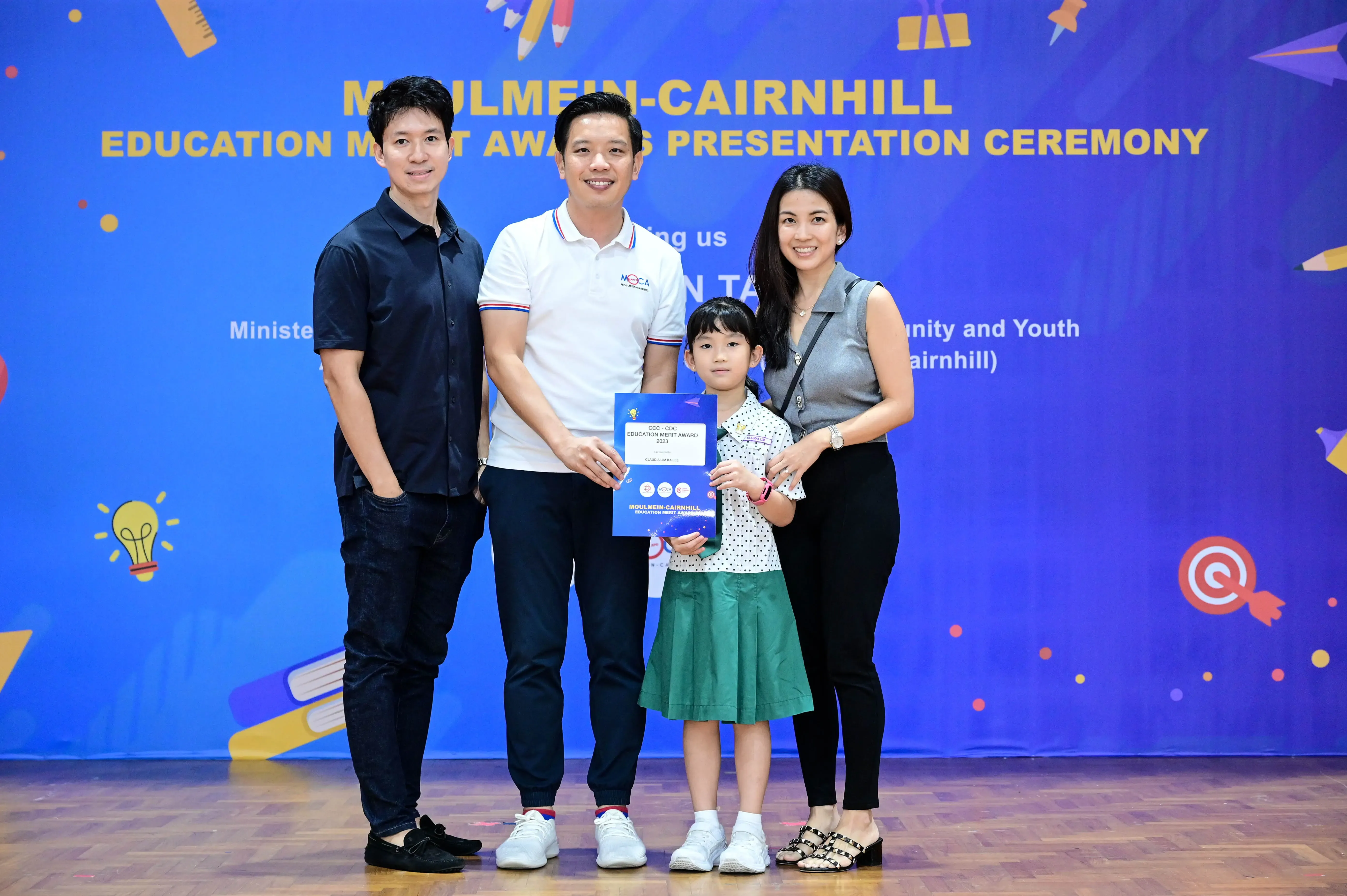 Three adults and a young girl holding a certificate at the Moulmein-Cairnhill Education Merit Awards Presentation Ceremony.