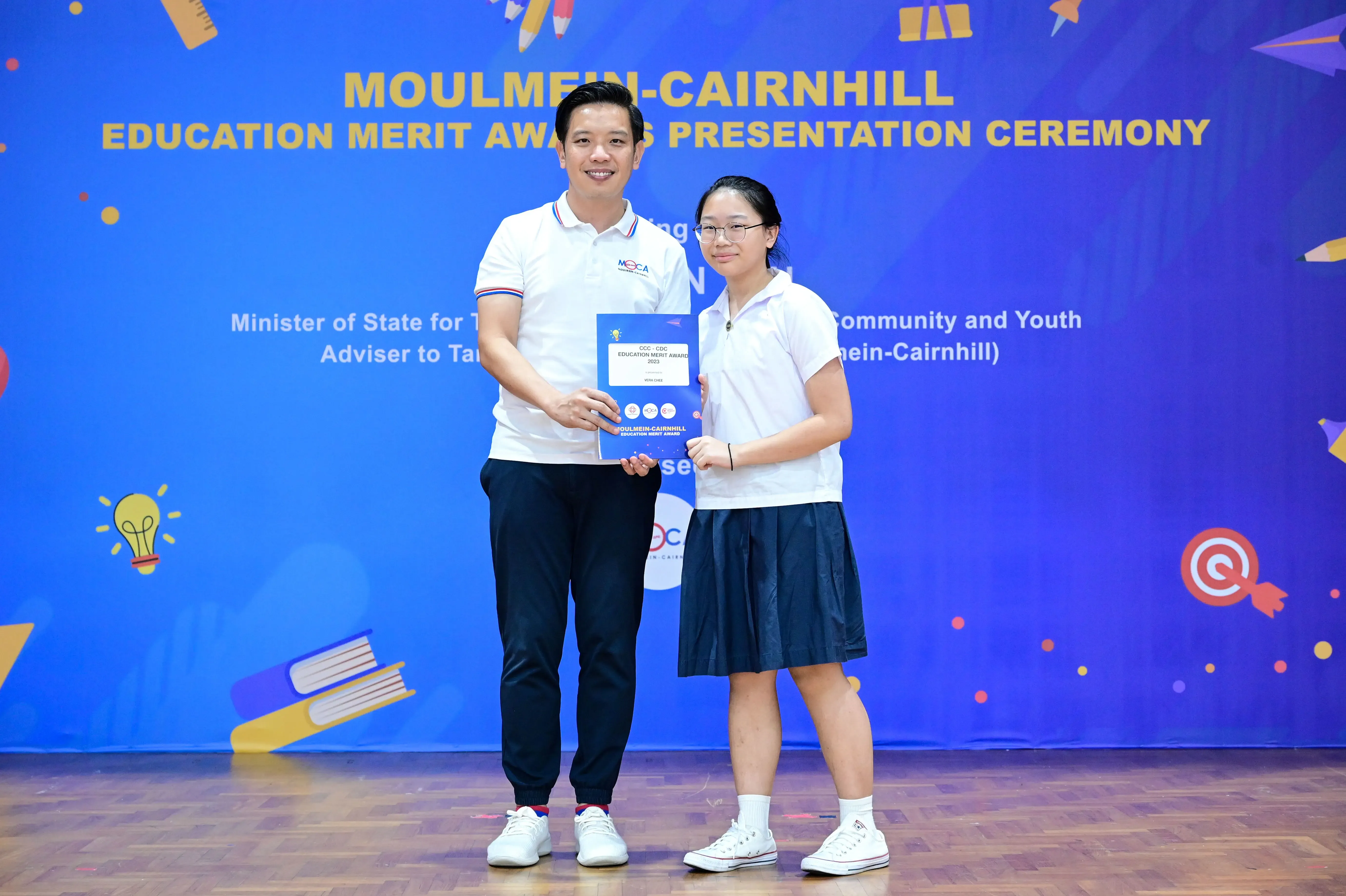A man and a young girl hold a certificate together at the Moulmein-Cairnhill Education Merit Awards ceremony.