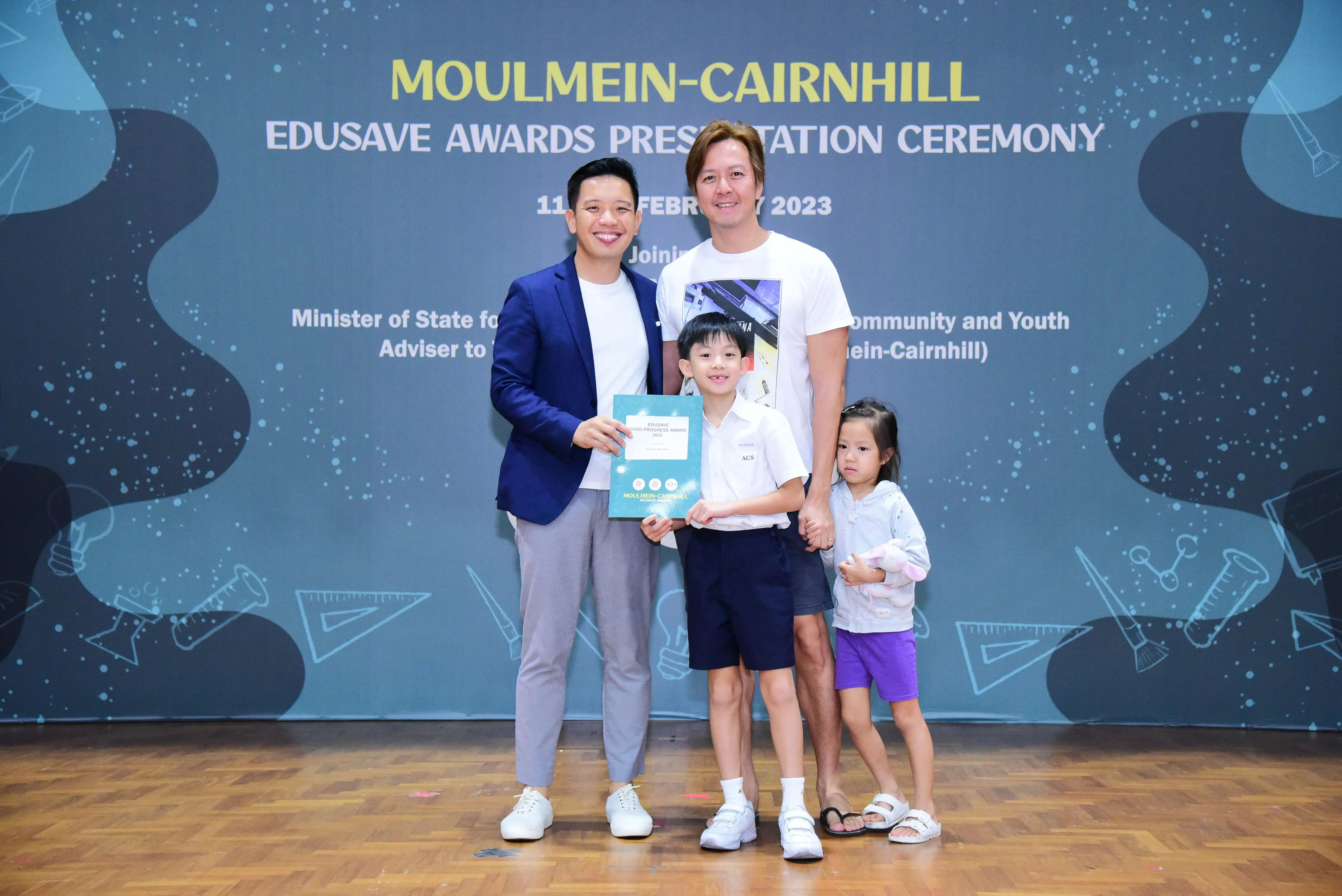 Two men, a boy holding a certificate, and a girl pose at the Moulmein-Cairnhill Edusave Awards Ceremony 2023.