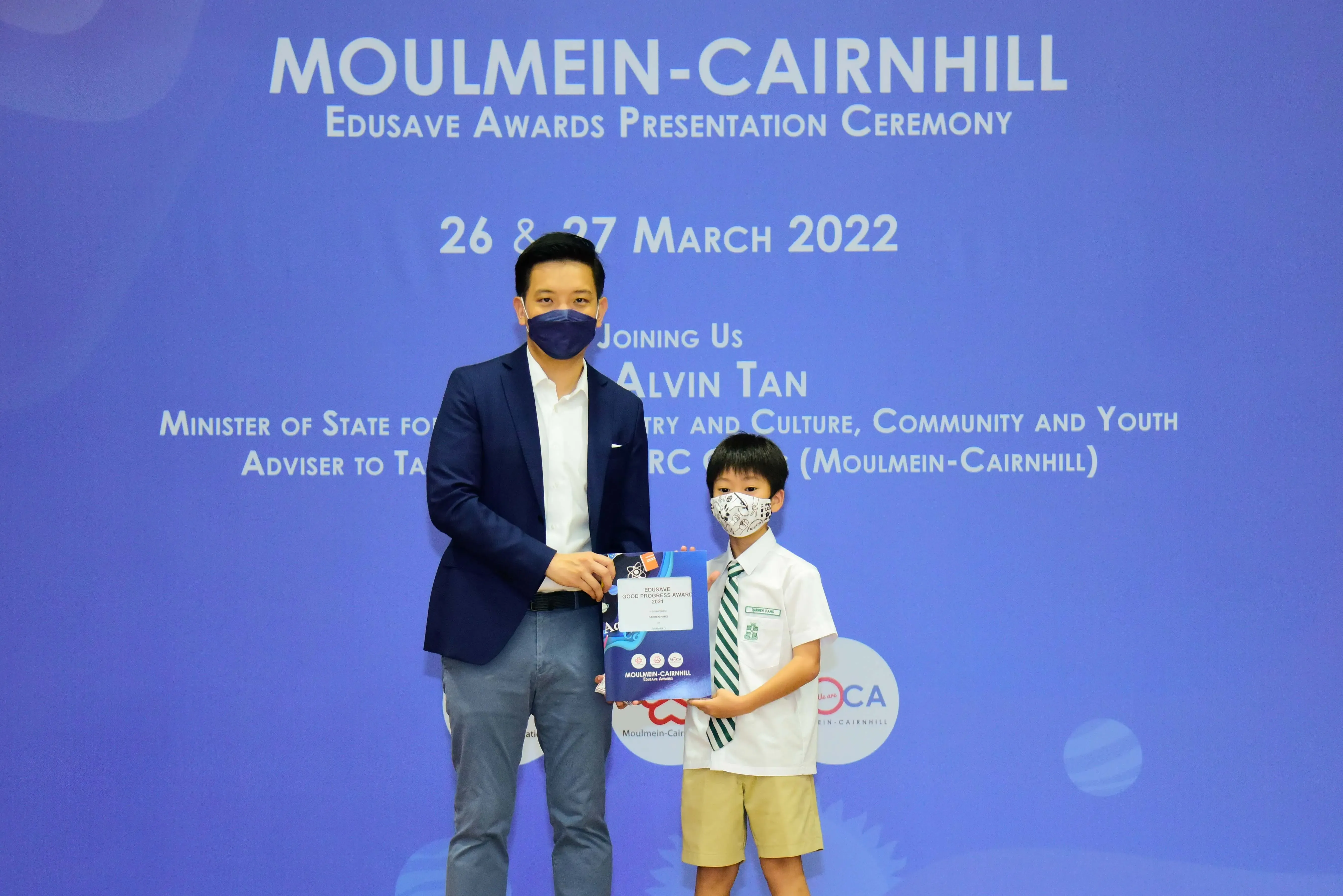 An adult and a young student in uniform hold an award at the Moulmein-Cairnhill Edusave Awards Ceremony, March 2022.