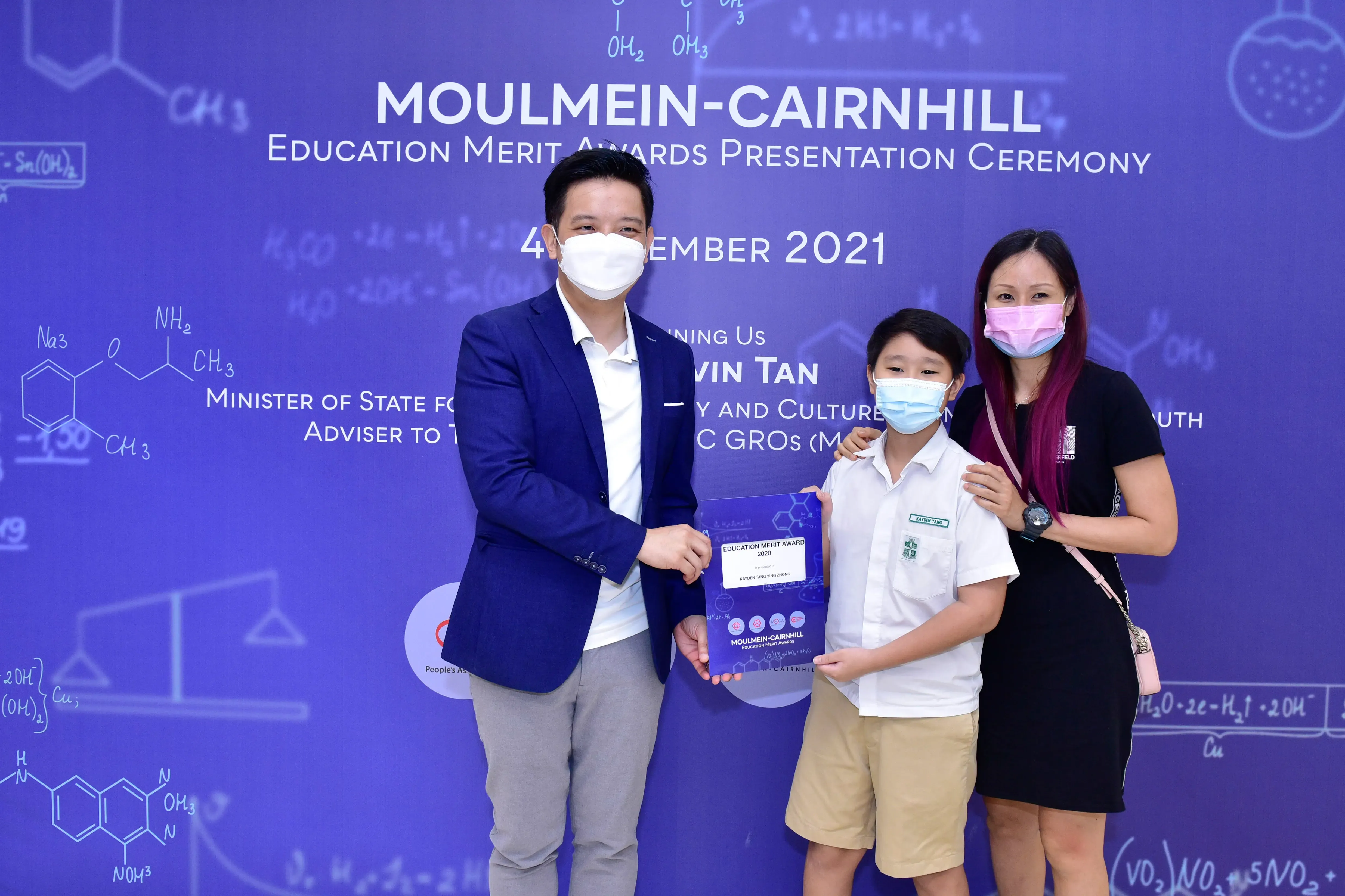 Three masked people pose with an award certificate at the Moulmein-Cairnhill Education Merit Awards Ceremony 2021.