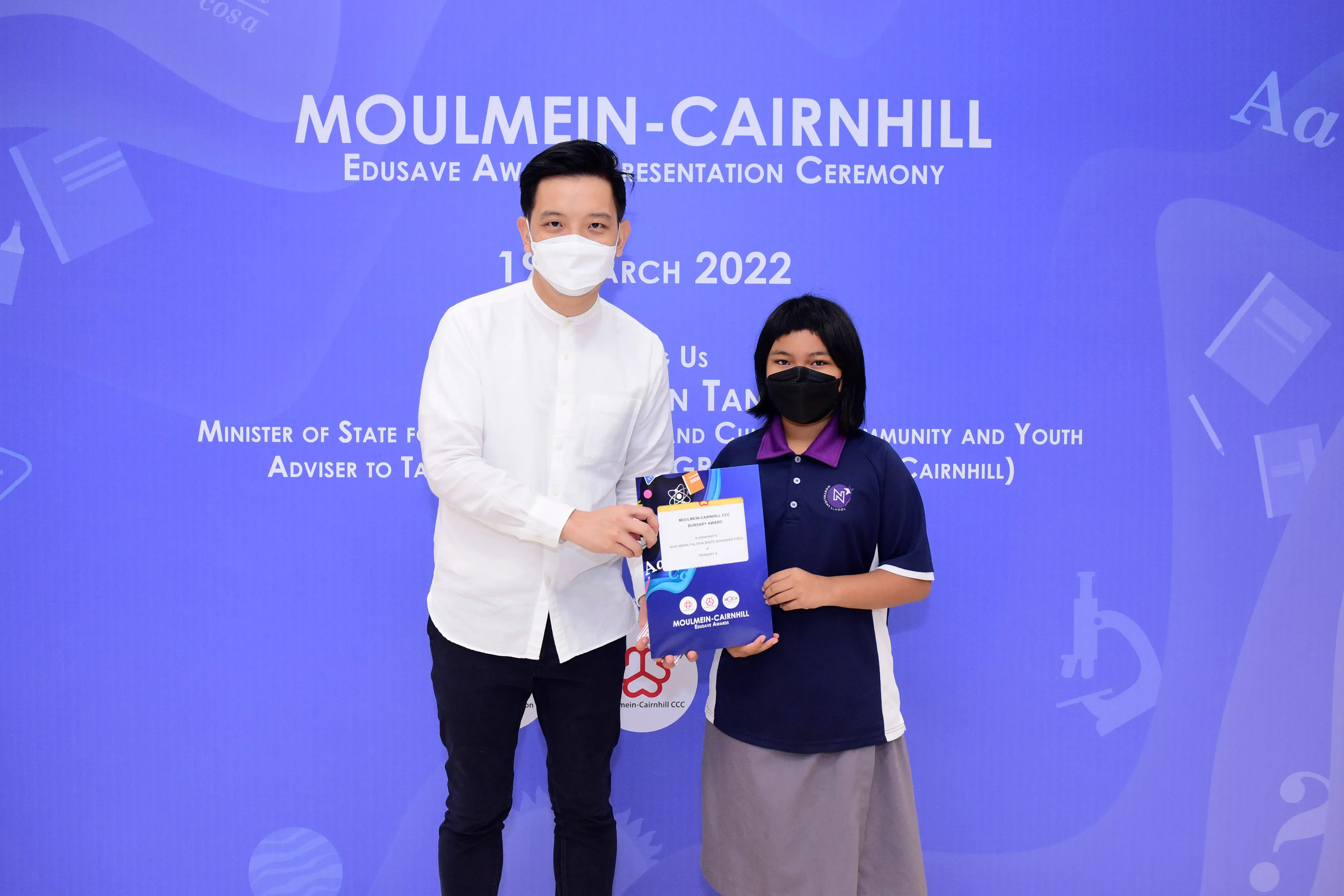 An adult and a young student hold an award certificate at the Moulmein-Cairnhill Edusave Ceremony, March 2022.