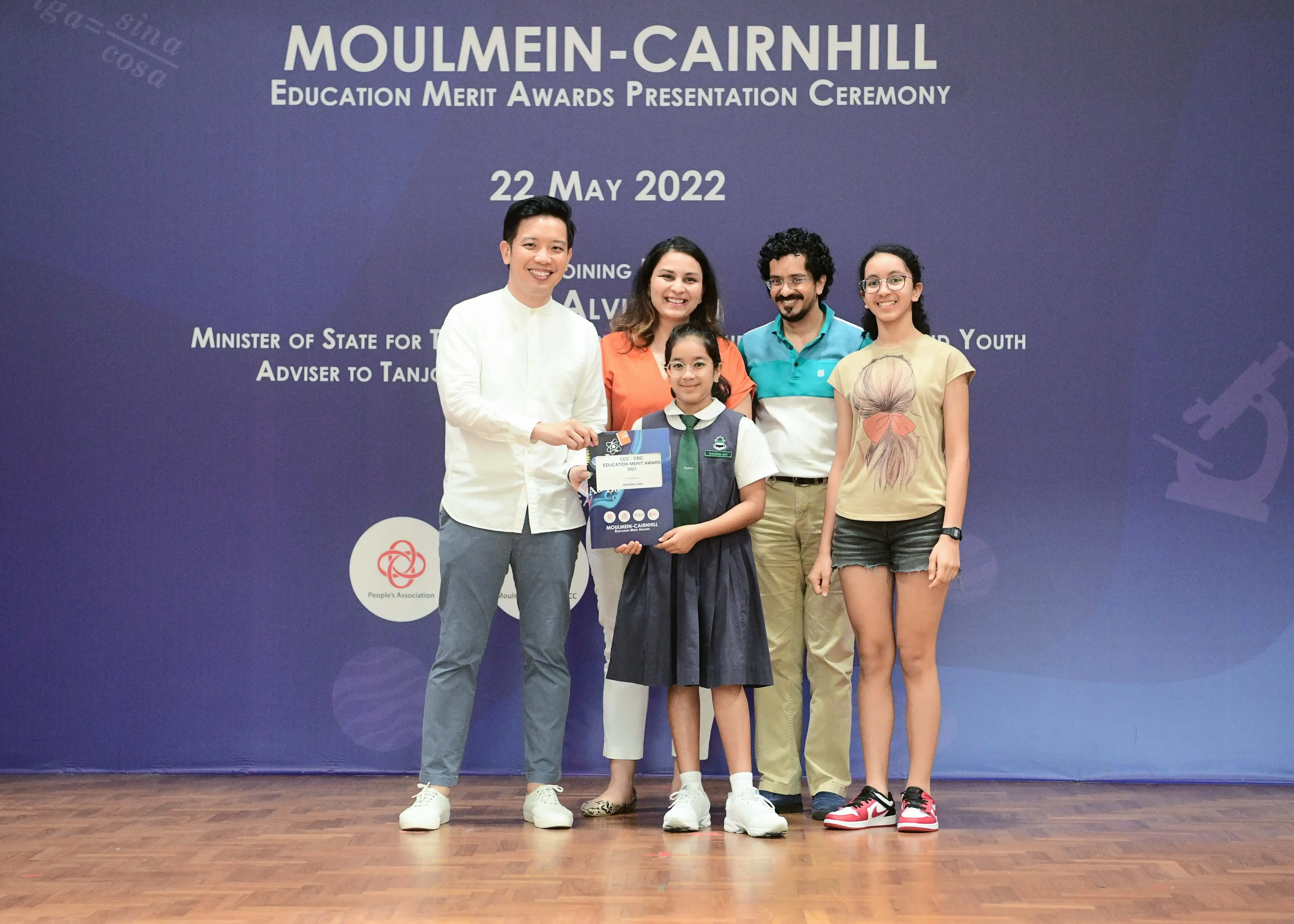 Five people pose at the Moulmein-Cairnhill Education Merit Awards Ceremony on 22 May 2022, with a girl holding an award.