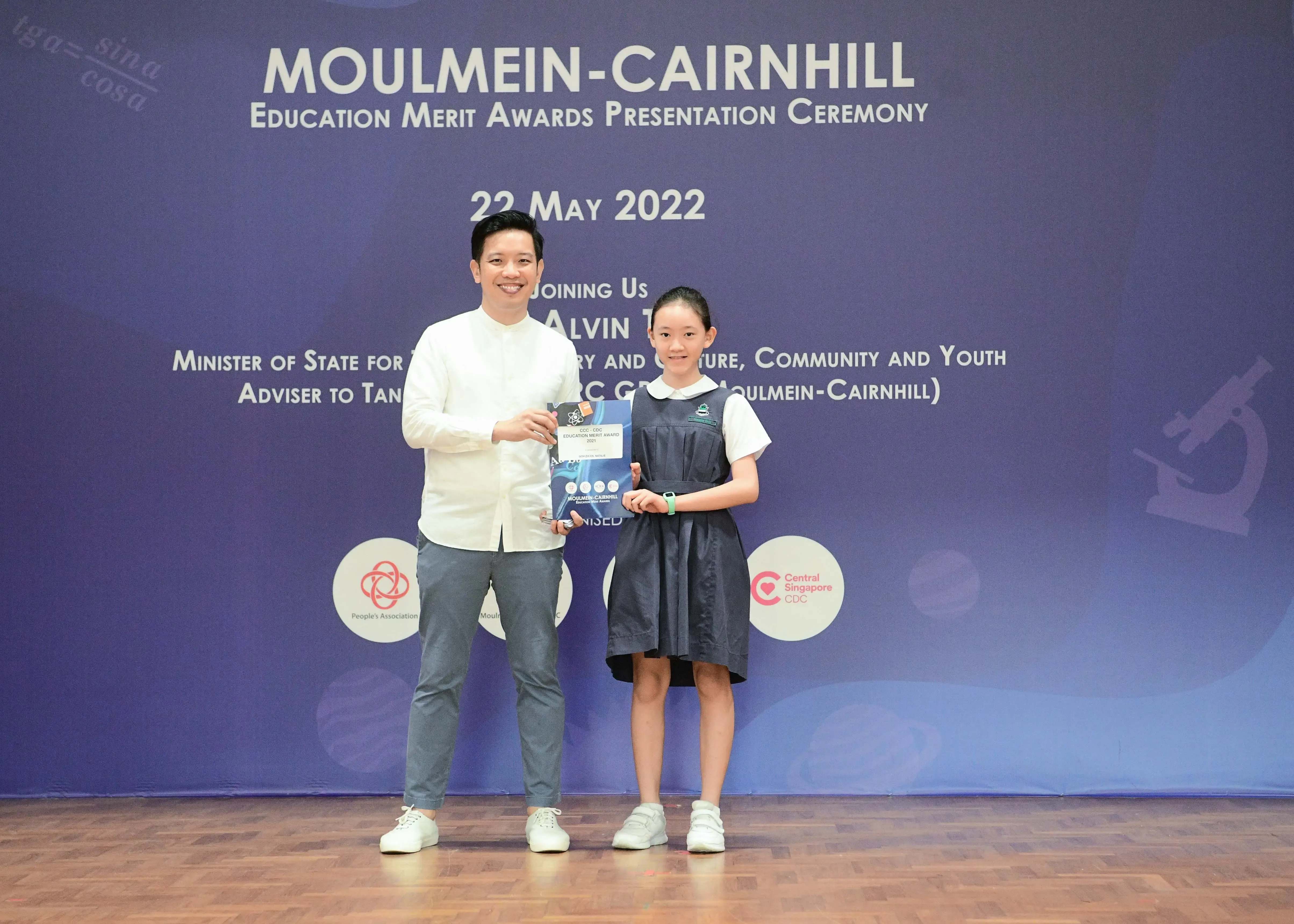 A man and a young girl in school uniform hold an award at the Moulmein-Cairnhill Education Merit Awards ceremony, May 2022.