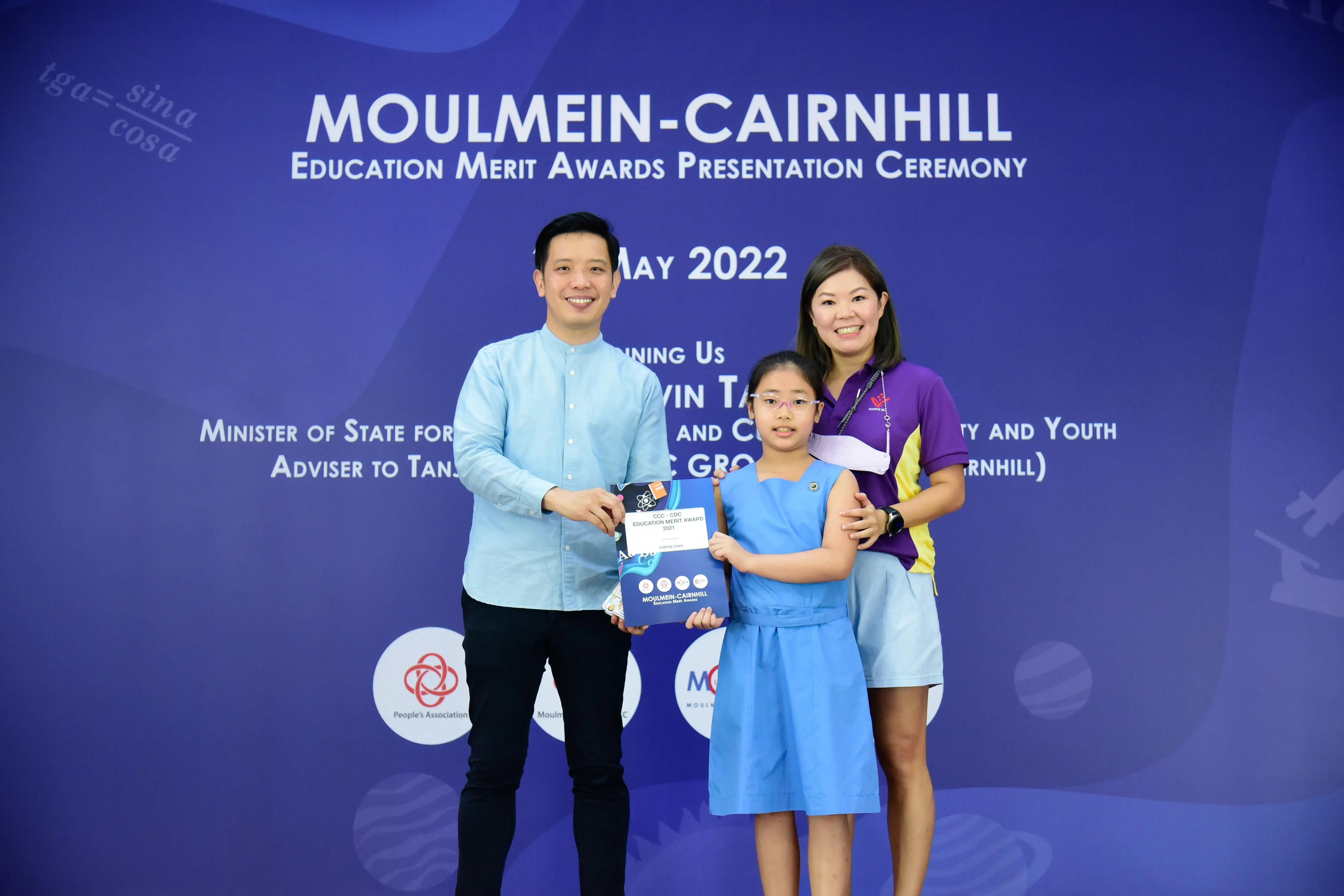 A man and woman stand with a young girl holding an award certificate at the Moulmein-Cairnhill Education Merit Awards 2022.