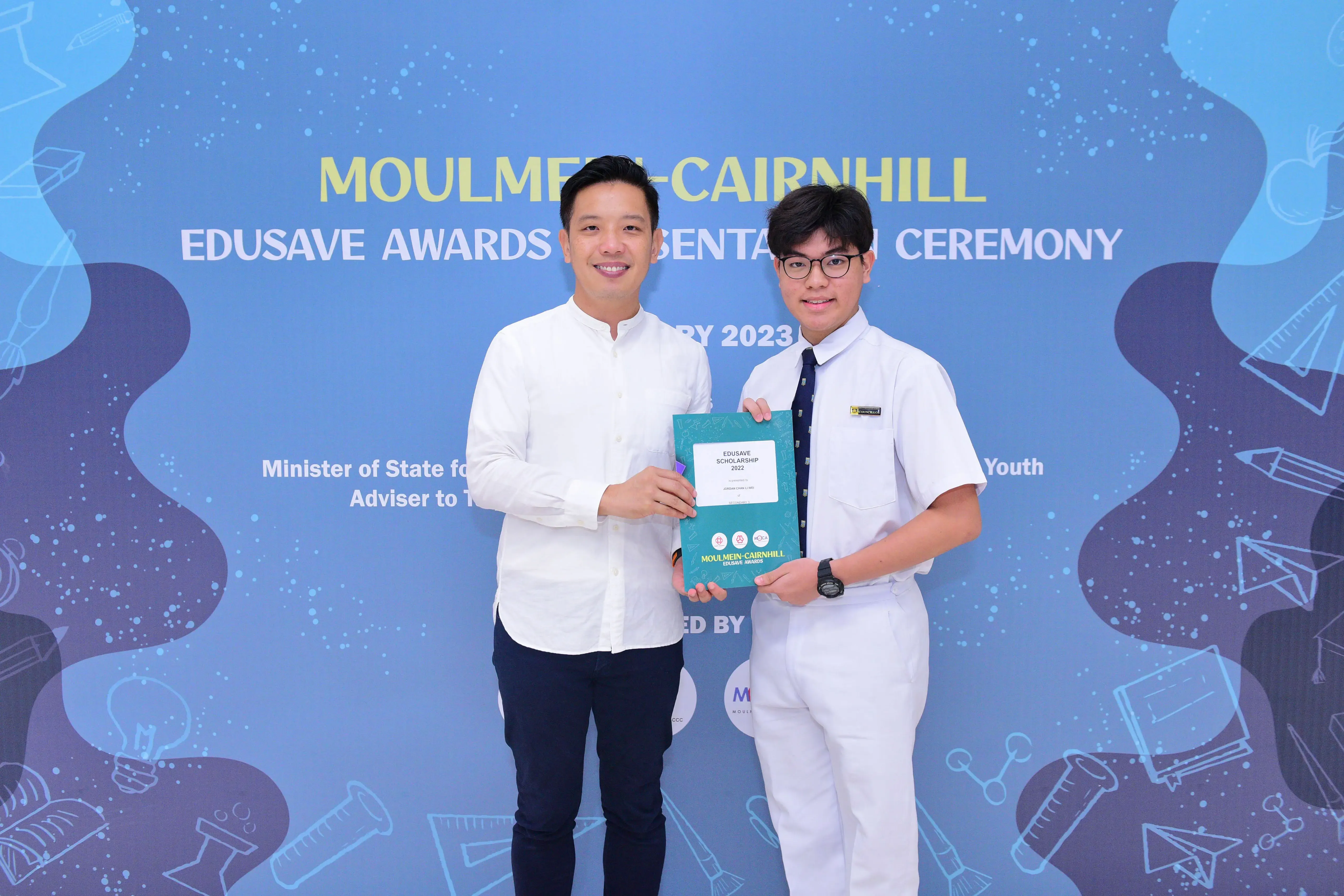 Two people hold a teal Edusave Scholarship certificate at the Moulmein-Cairnhill Edusave Awards Ceremony 2023.