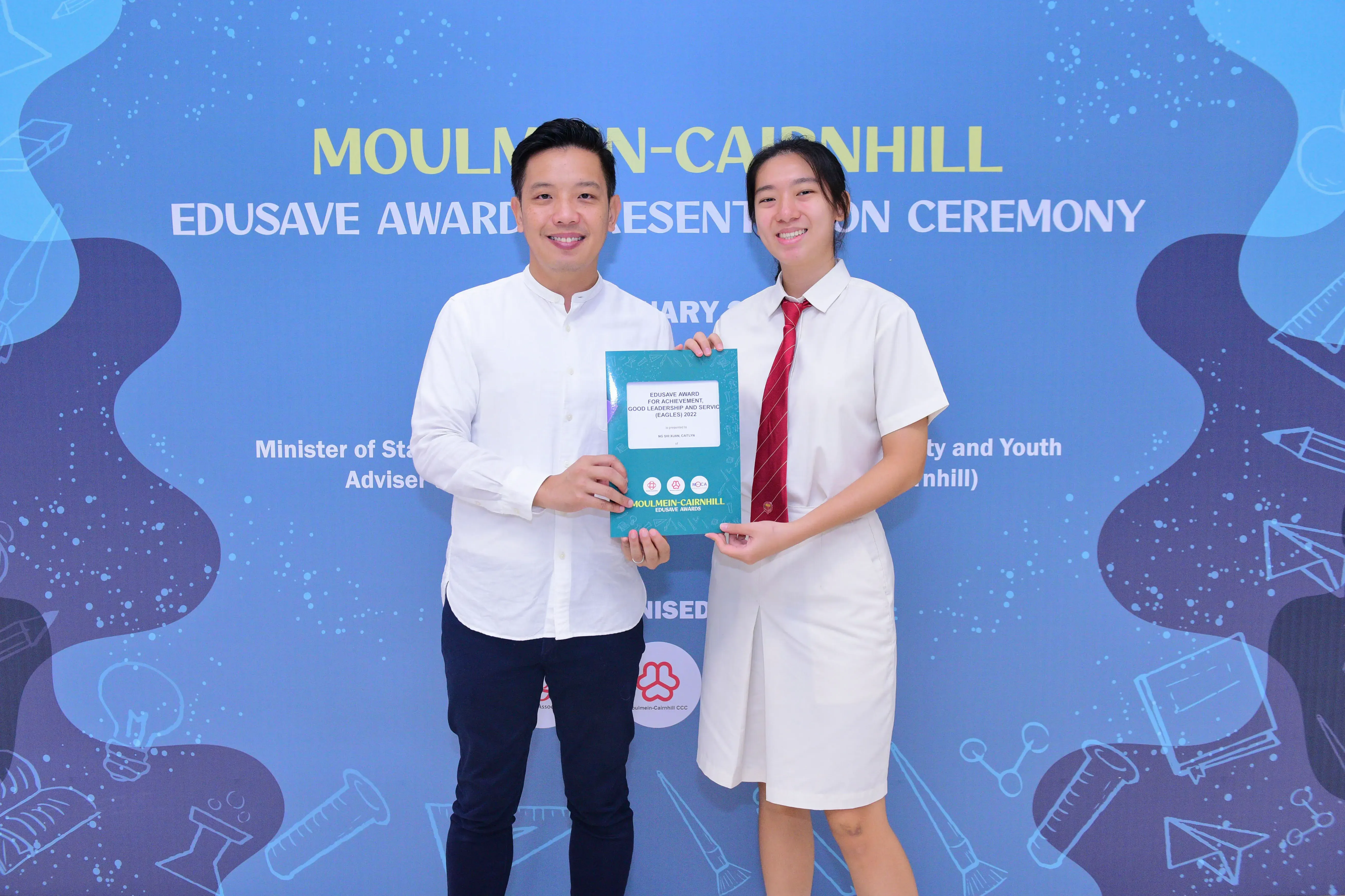 Two people smiling and holding an Edusave award certificate at the Moulmein-Cairnhill Edusave Award Presentation Ceremony.