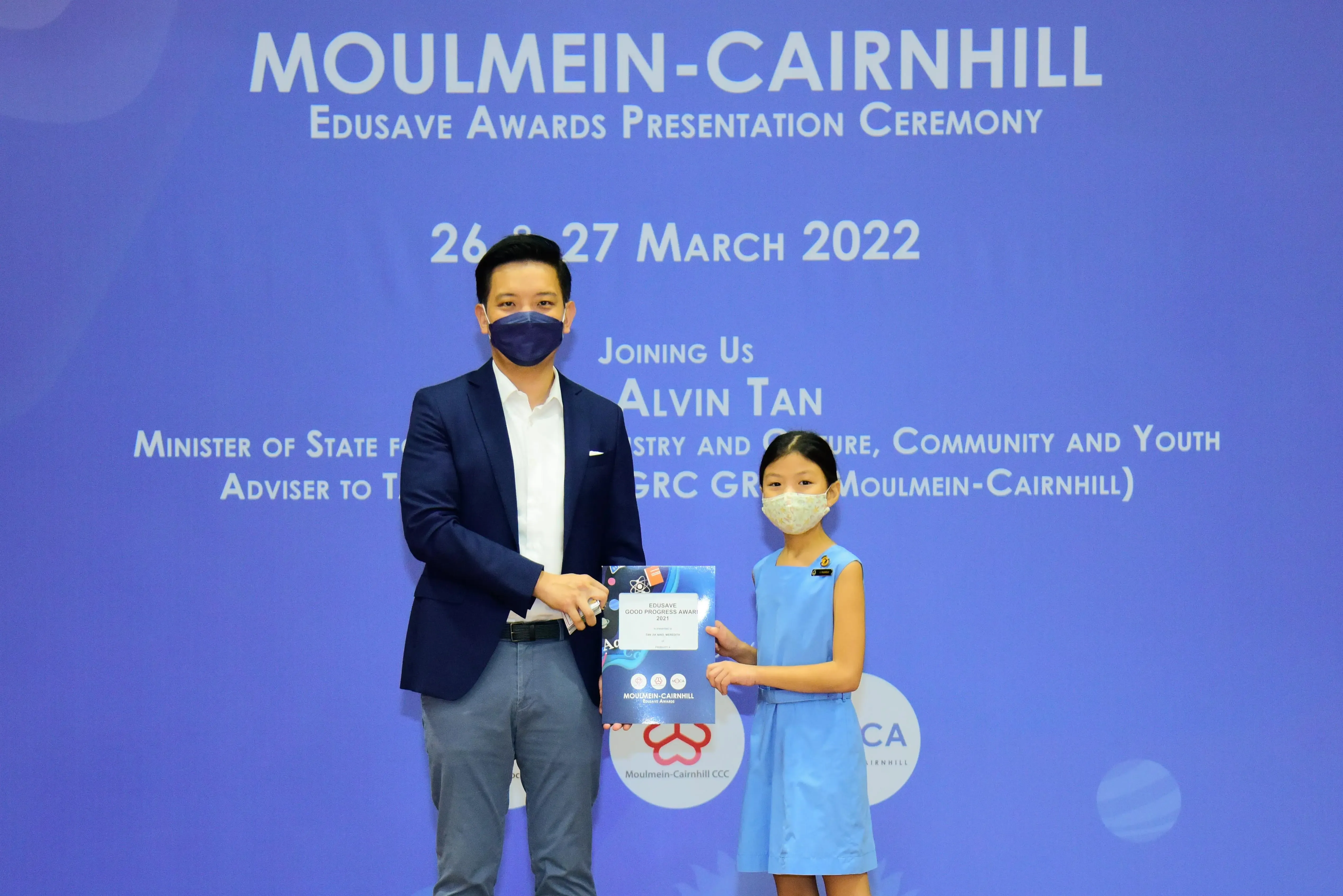 A masked man and young girl hold an award certificate at the Moulmein-Cairnhill Edusave Awards Ceremony, March 2022.